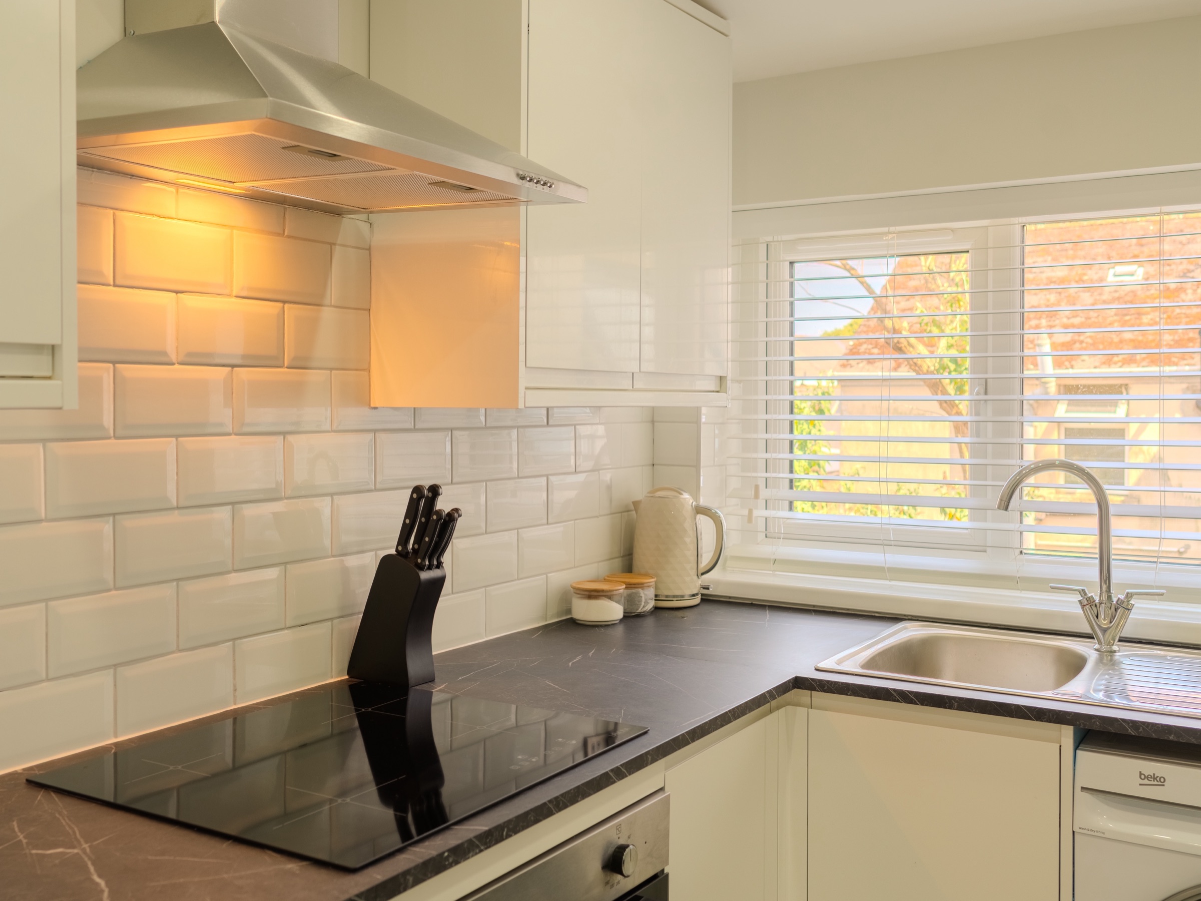 A galley kitchen with white metro tiles, a dark stone worktop and a window over the sink
