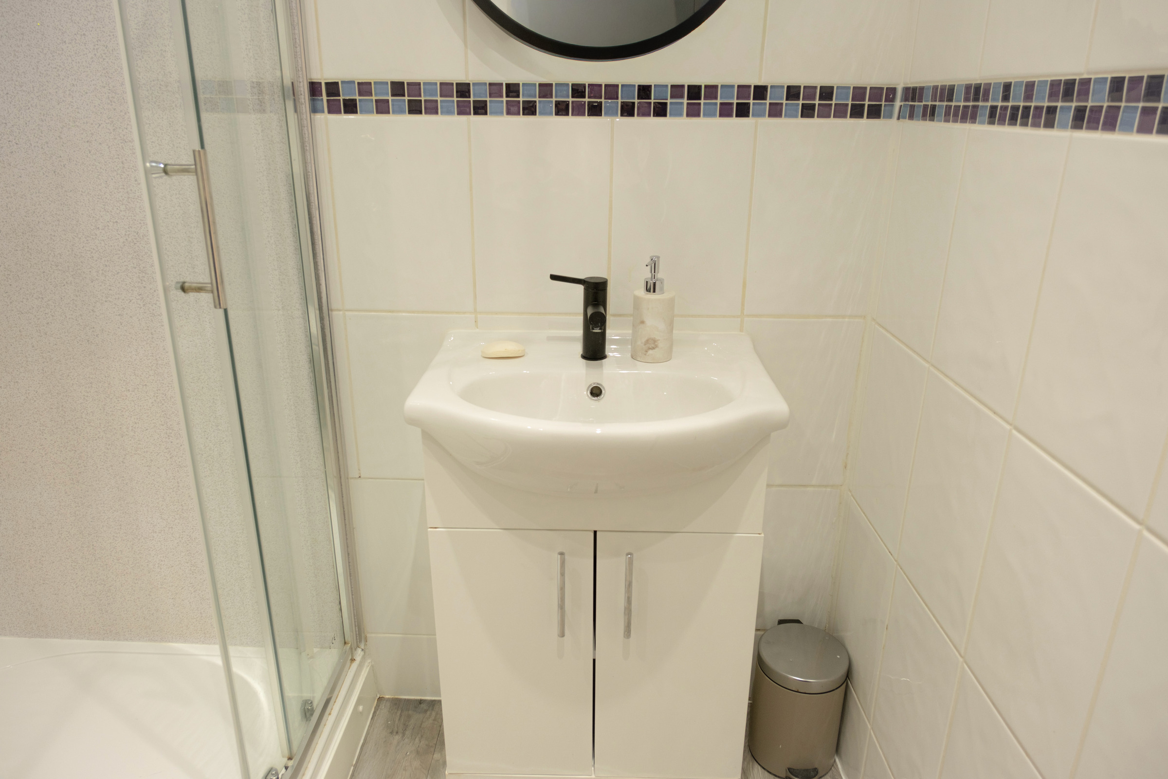 White basin with a black tap and compact storage in the shower room.