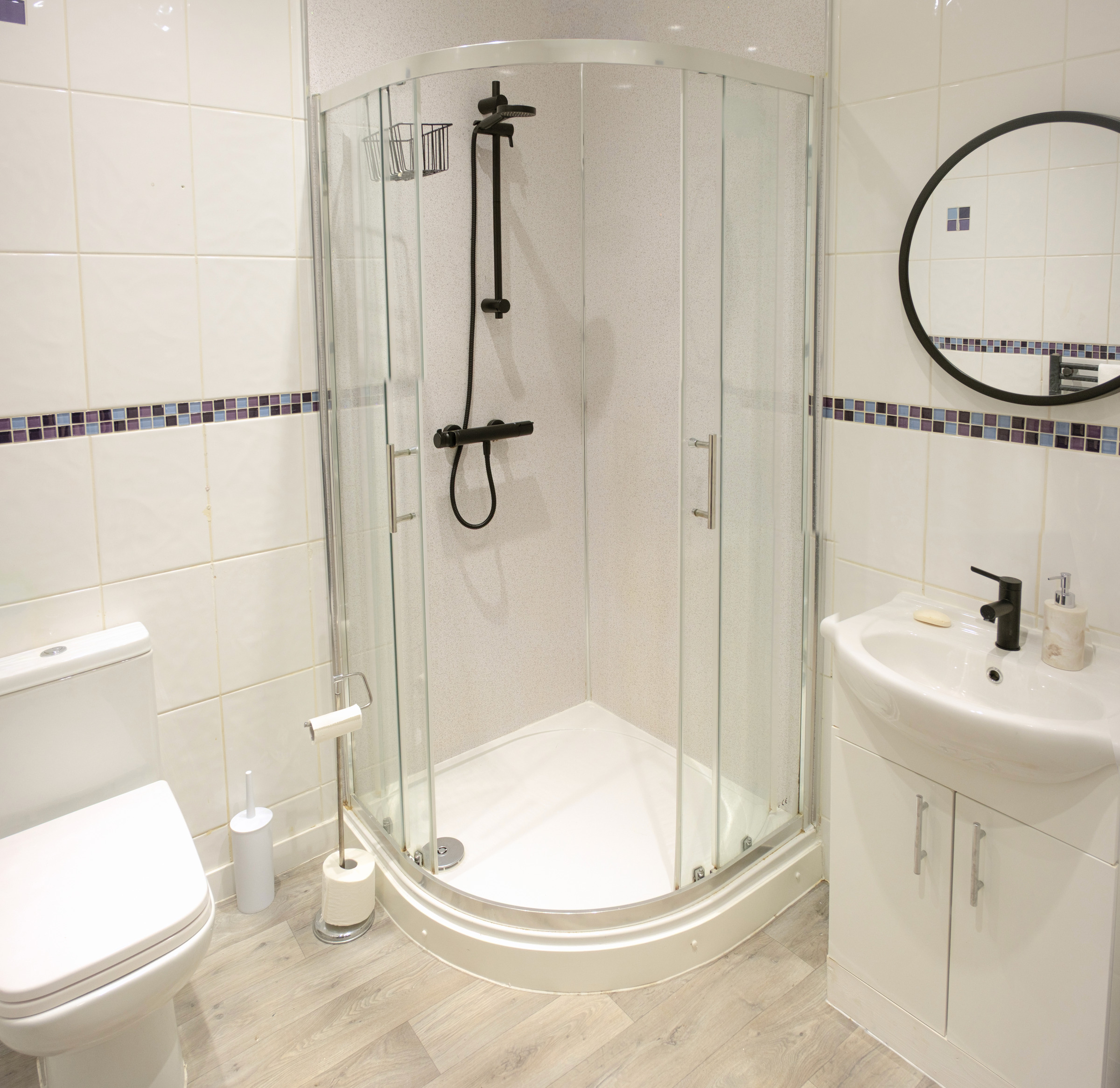 Full view of a compact shower room with glass enclosure, white basin and black fittings.