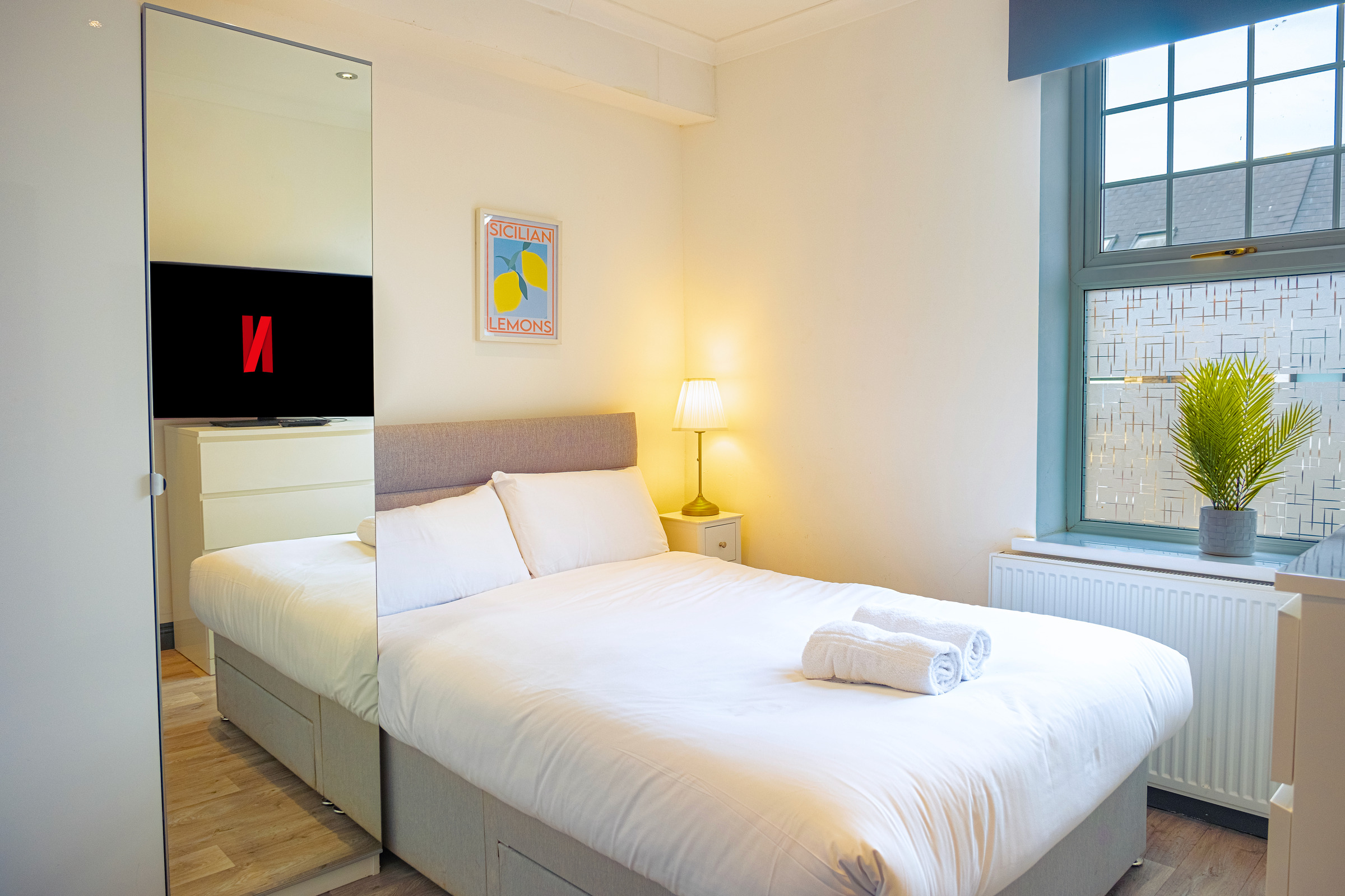 White double bed and bedside lamp beside a patterned-glass bedroom window.