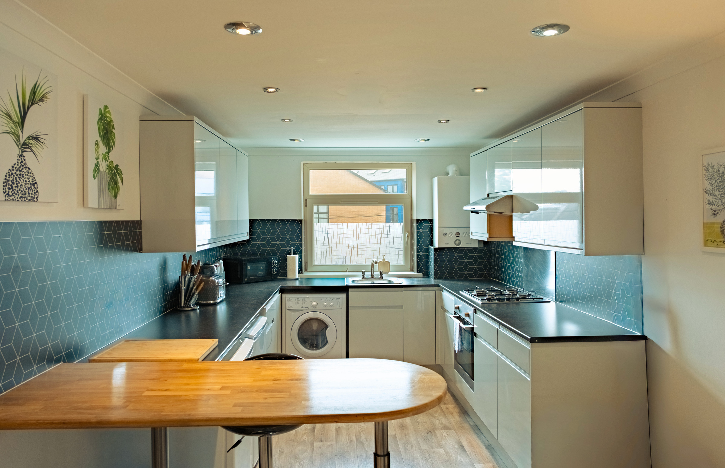Pale fitted kitchen with wood worktops, blue patterned splashback and a washing machine.