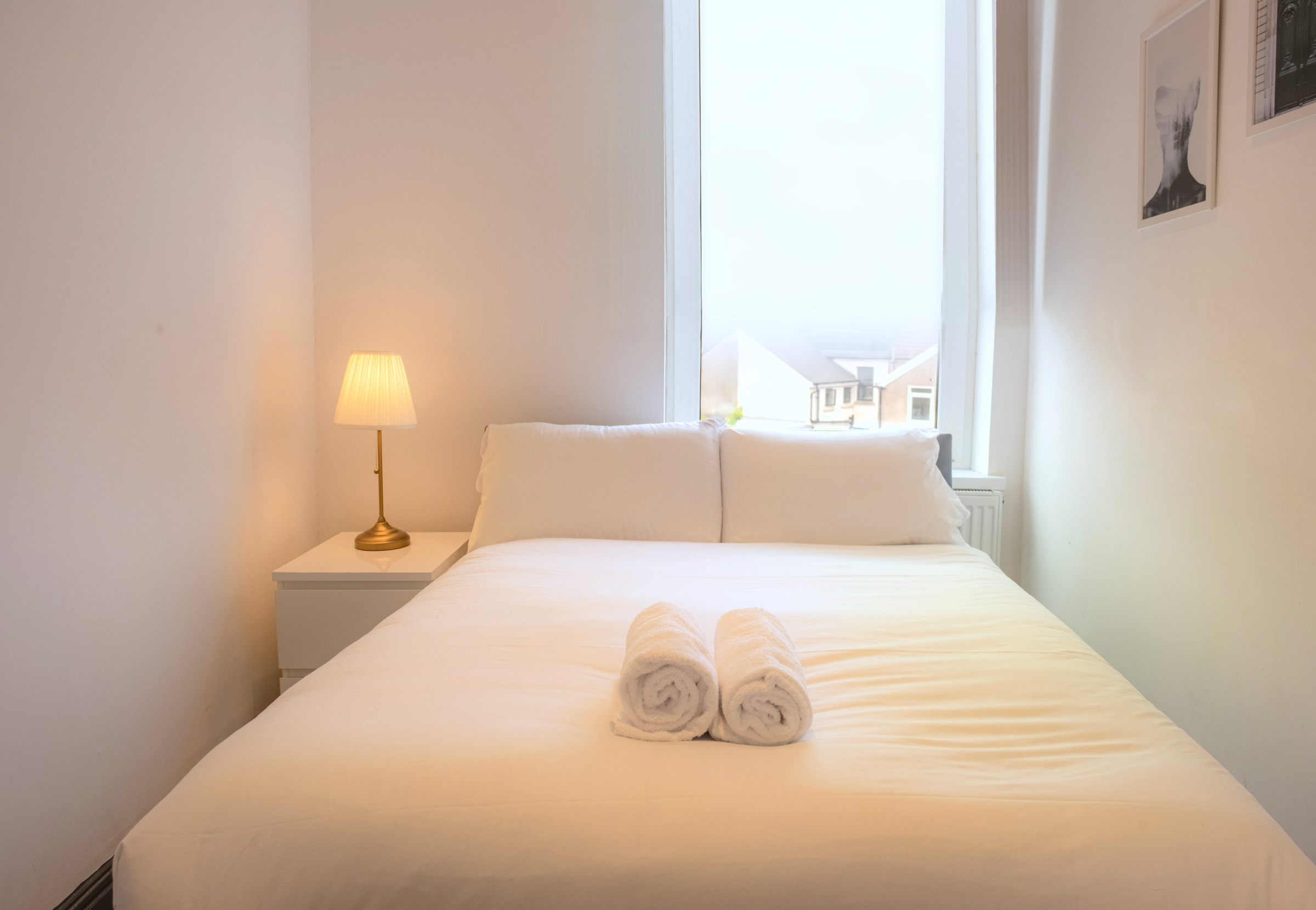 White bed linen and a warm bedside lamp beneath a bright bedroom window.