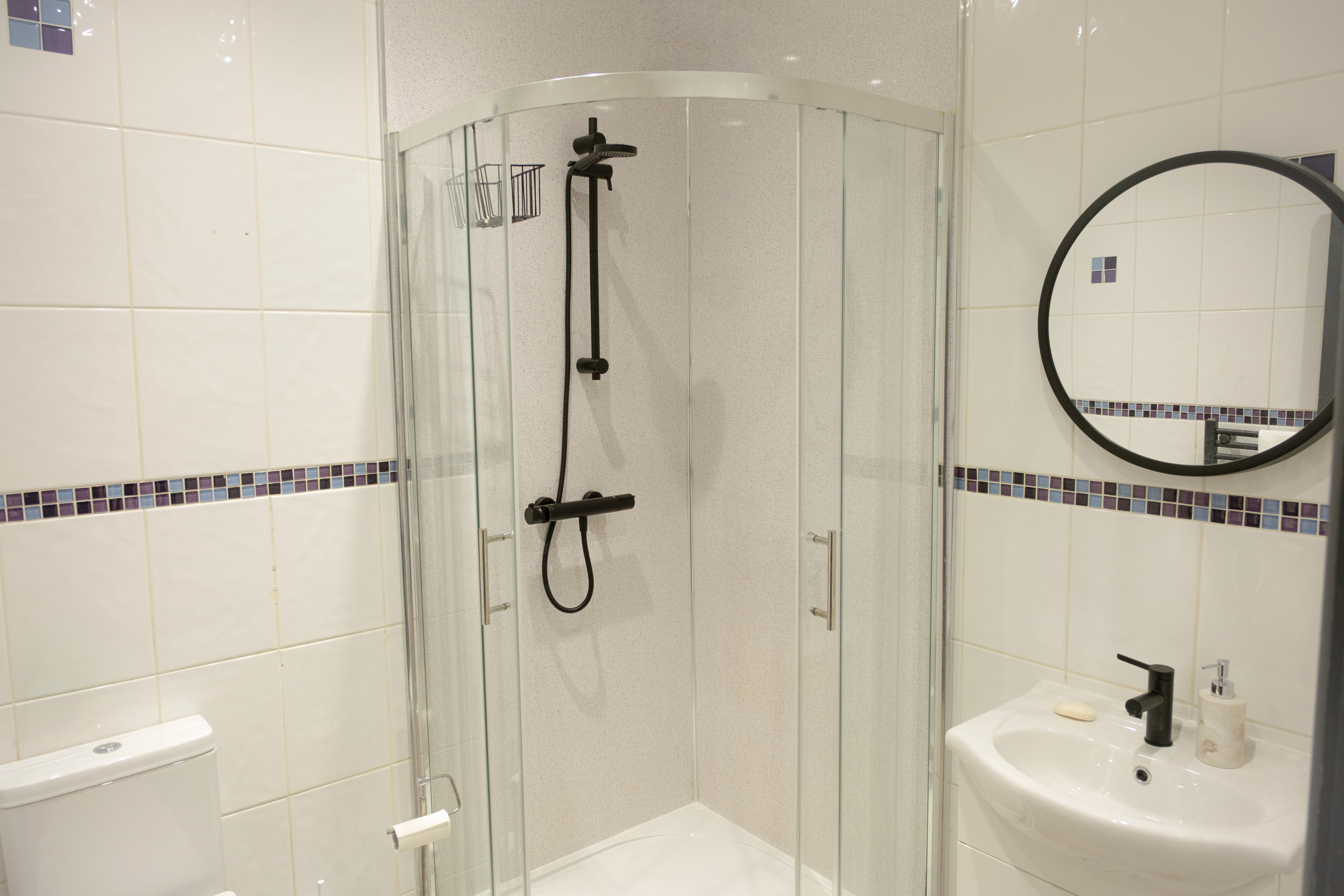 Black shower fittings, glass screen and a round mirror in the tiled bathroom.