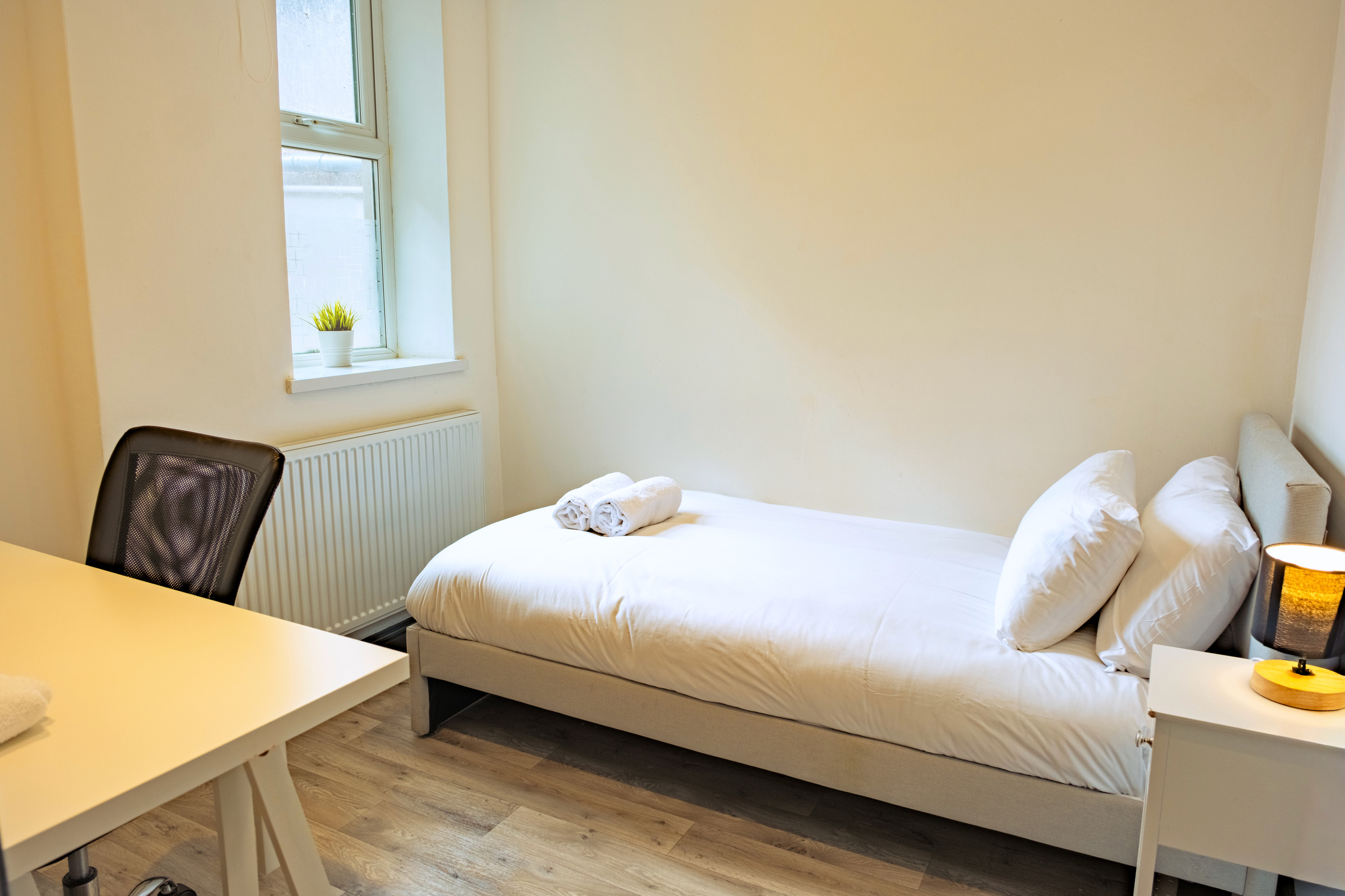 Single bed and work desk beside a bedroom window.