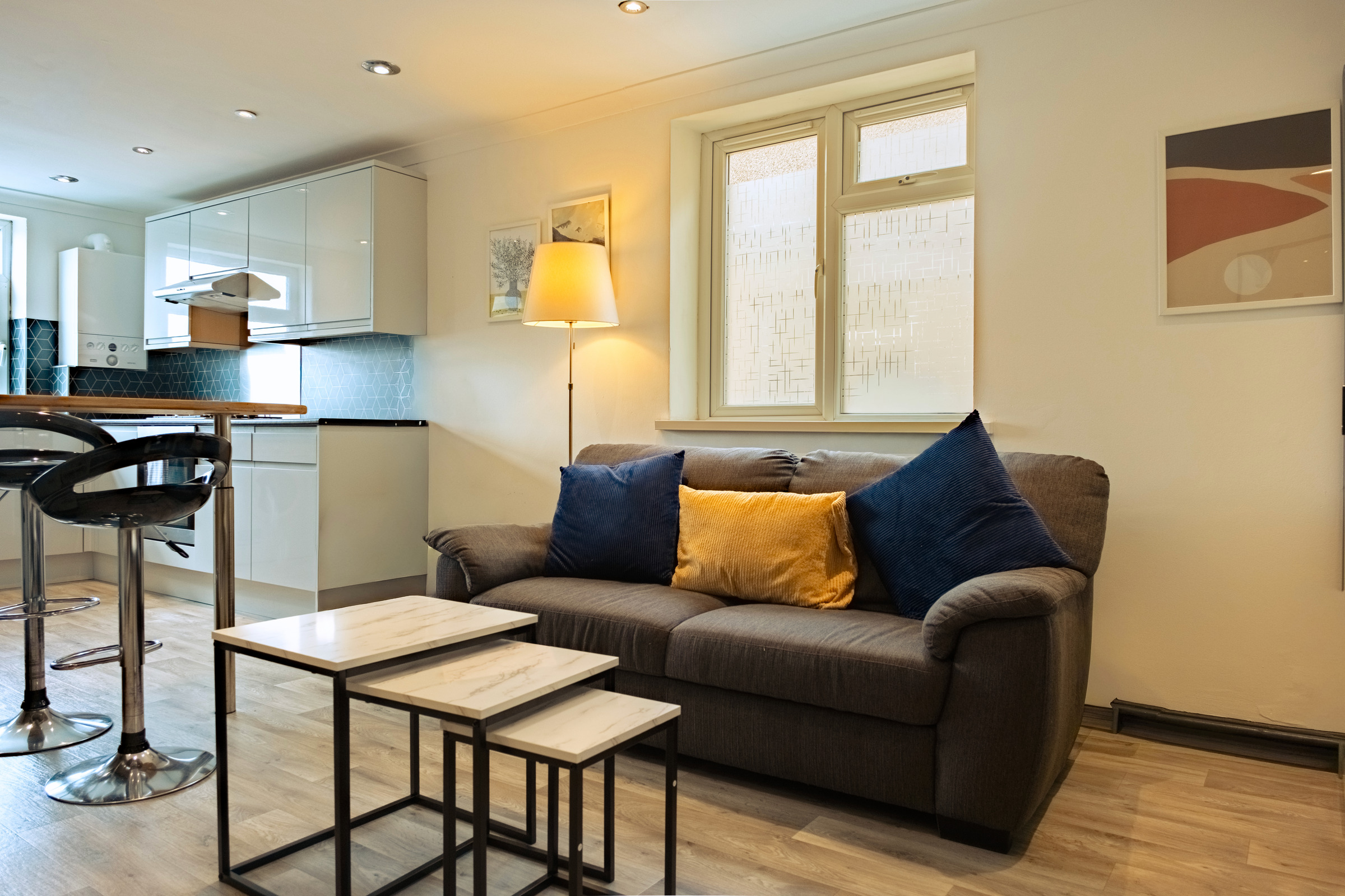 Grey sofa, blue and yellow cushions and three nesting tables beside the kitchenette.