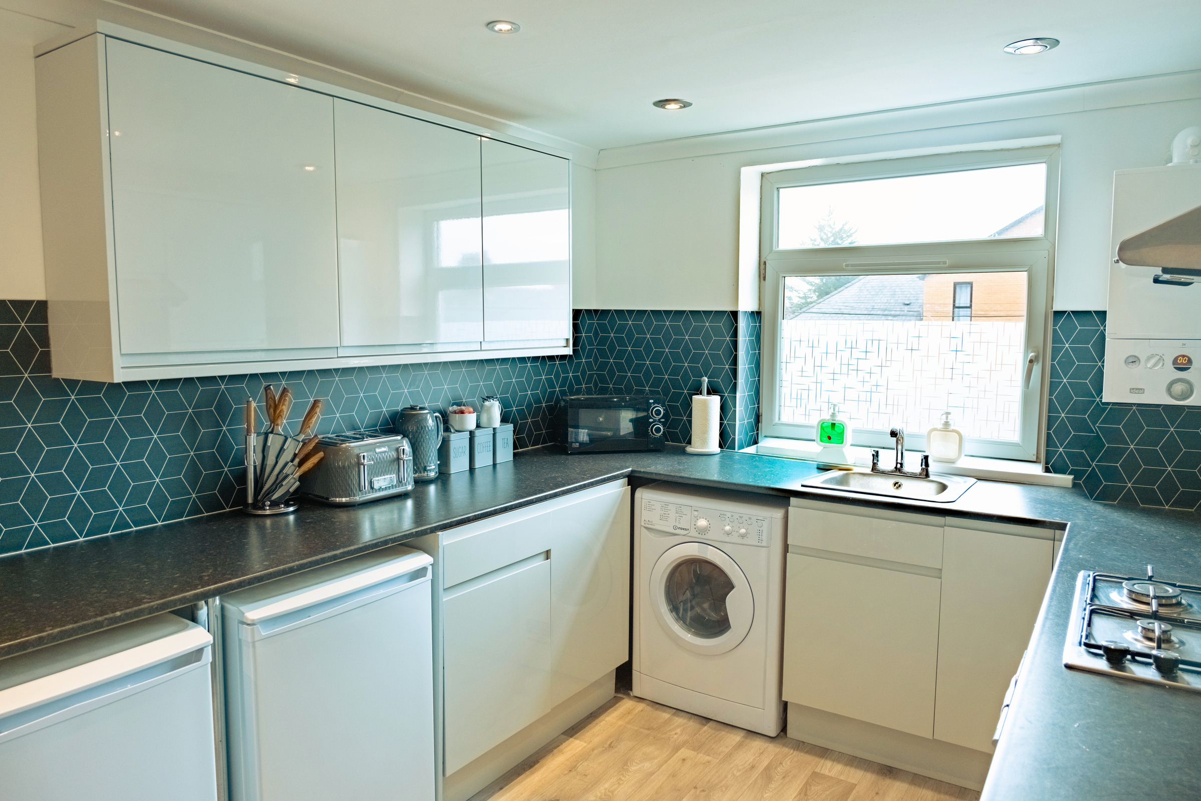 Working side of the fitted kitchenette with hob, oven, sink and patterned tiles.