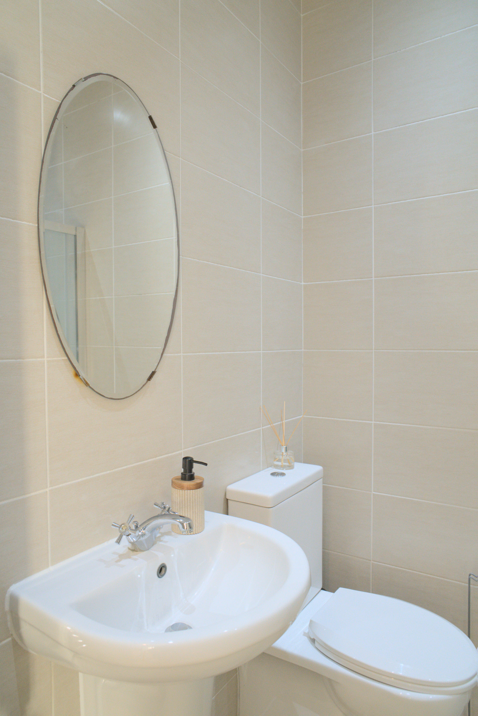 A compact bathroom with a white basin, round mirror and tiled wall.