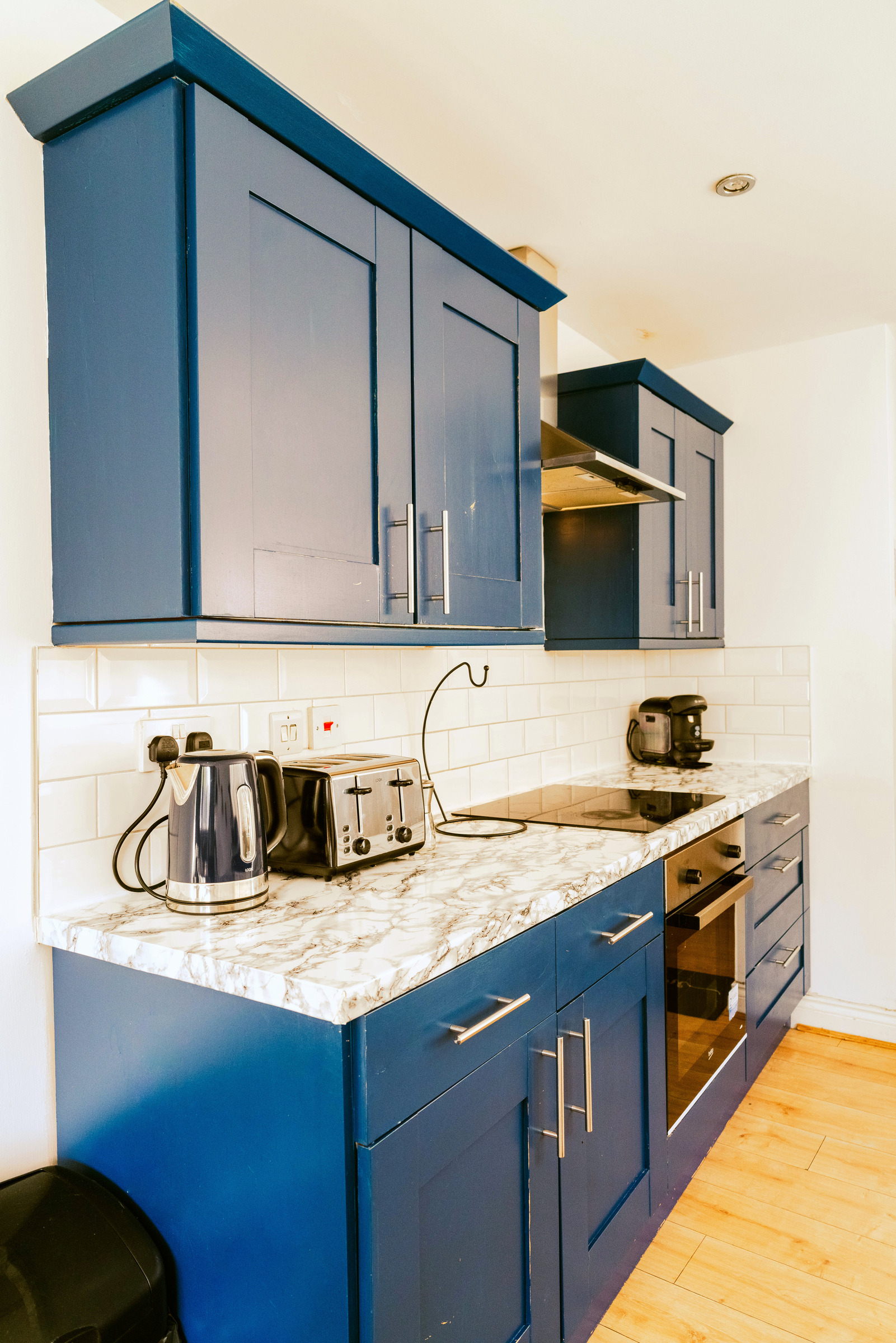 Blue kitchen cabinets, wood worktops and white splashback tiles in a compact fitted kitchen.