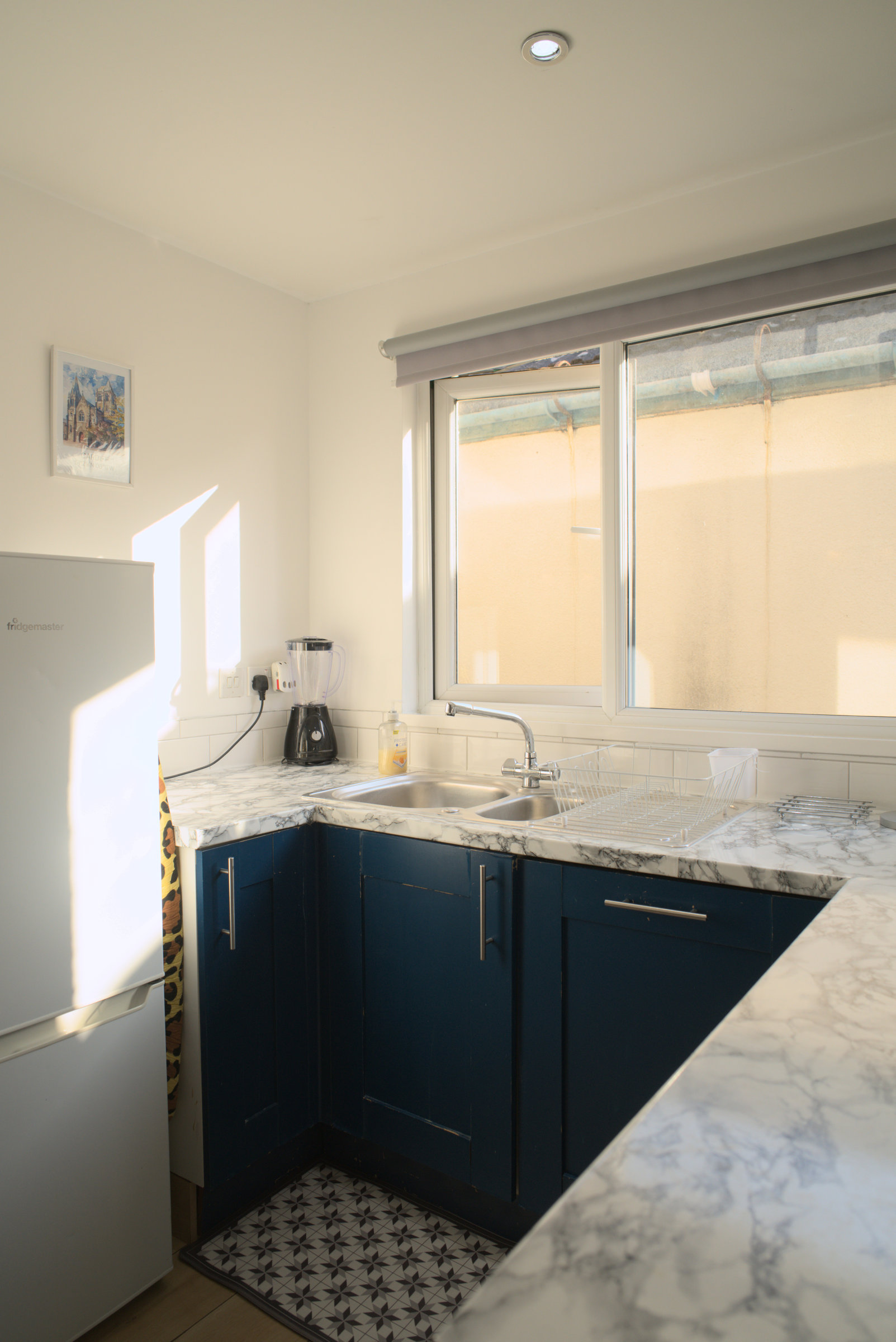 Blue kitchen cabinetry and a marble-pattern worktop beside a sunny window.