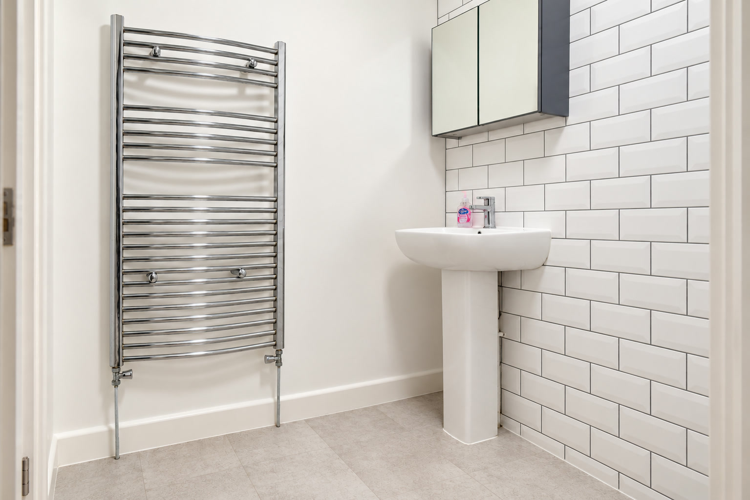 A pedestal basin, mirrored cabinet and chrome towel radiator against white metro tiles.