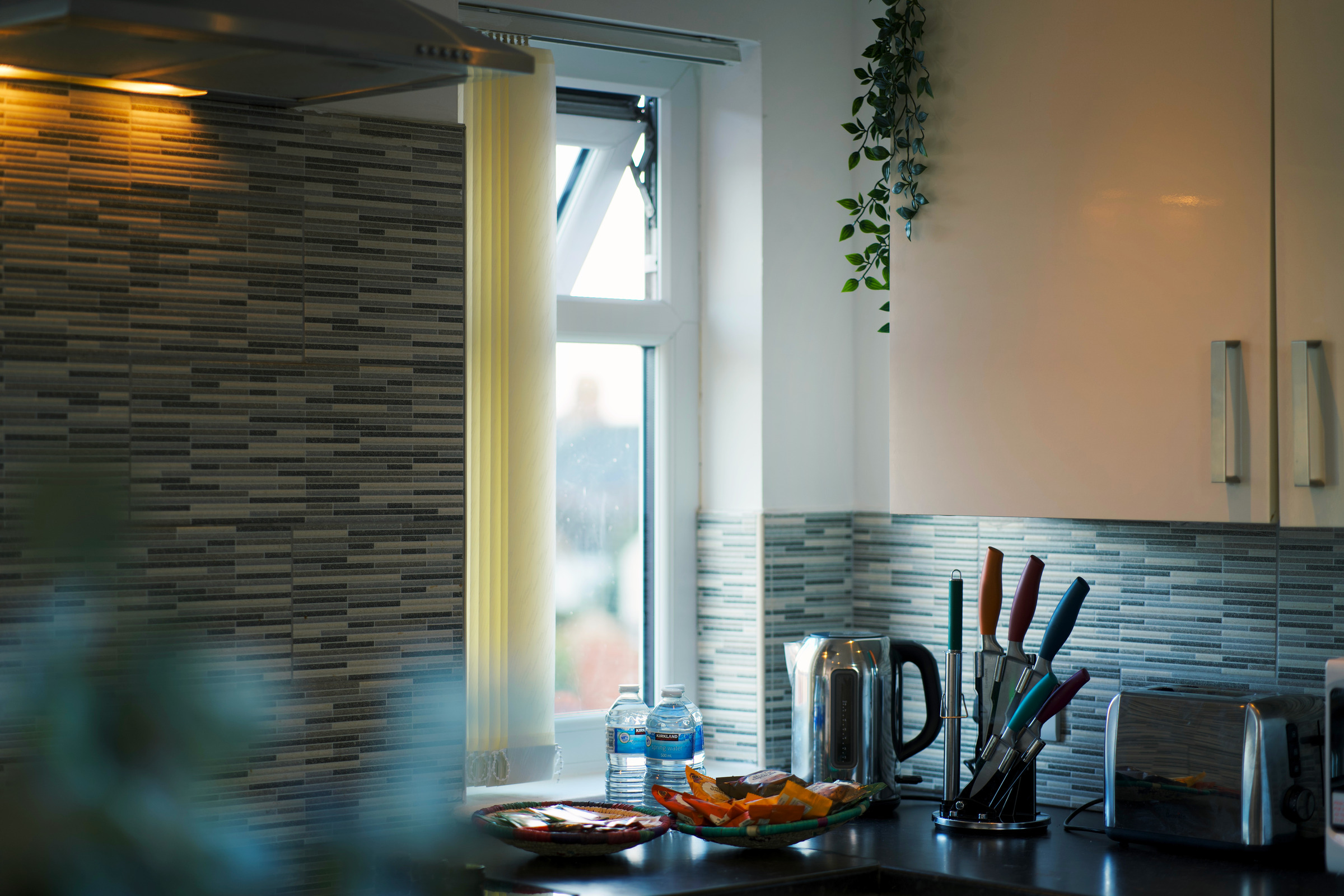 Wood kitchen worktop, textured splashback and utensils beside a daylight window.