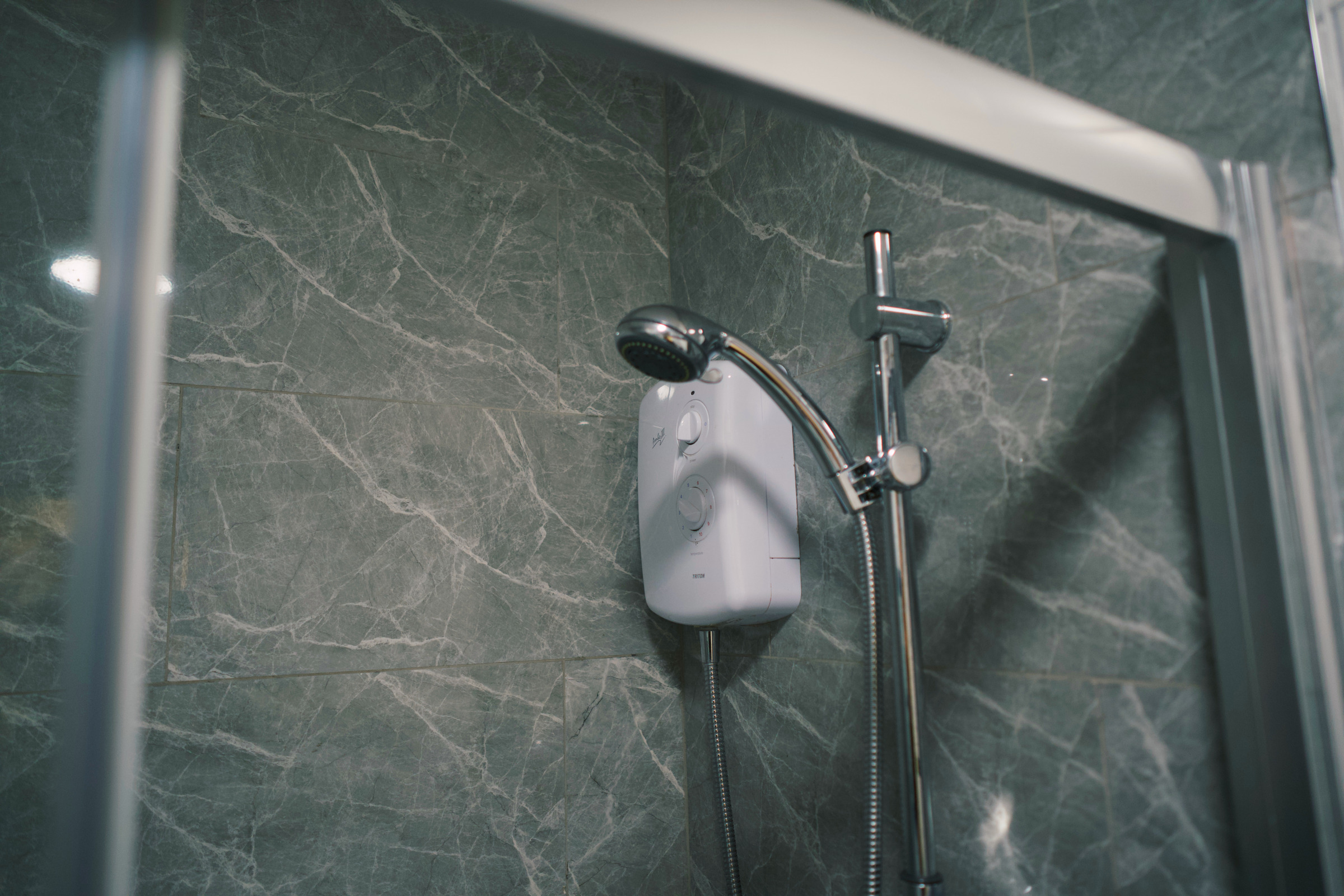 Chrome showerhead and rail against dark stone-pattern wall tiles.