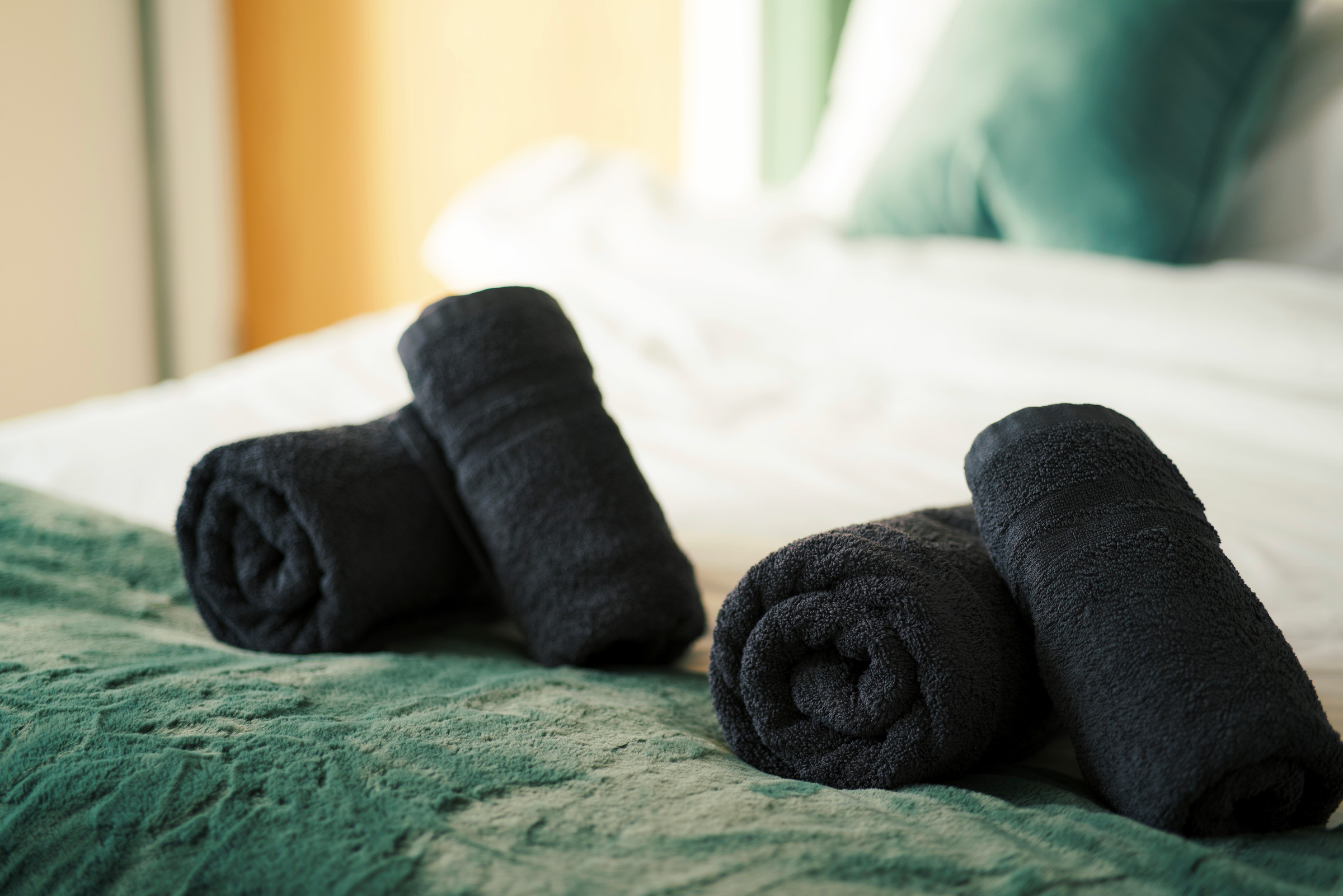 Rolled charcoal towels on textured green bed linen with soft light behind.