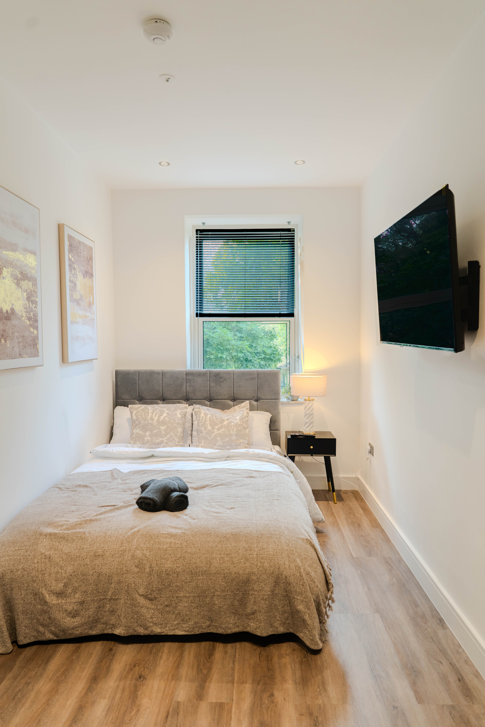 Made double bed beneath a window, with a round wall mirror and television to the side.