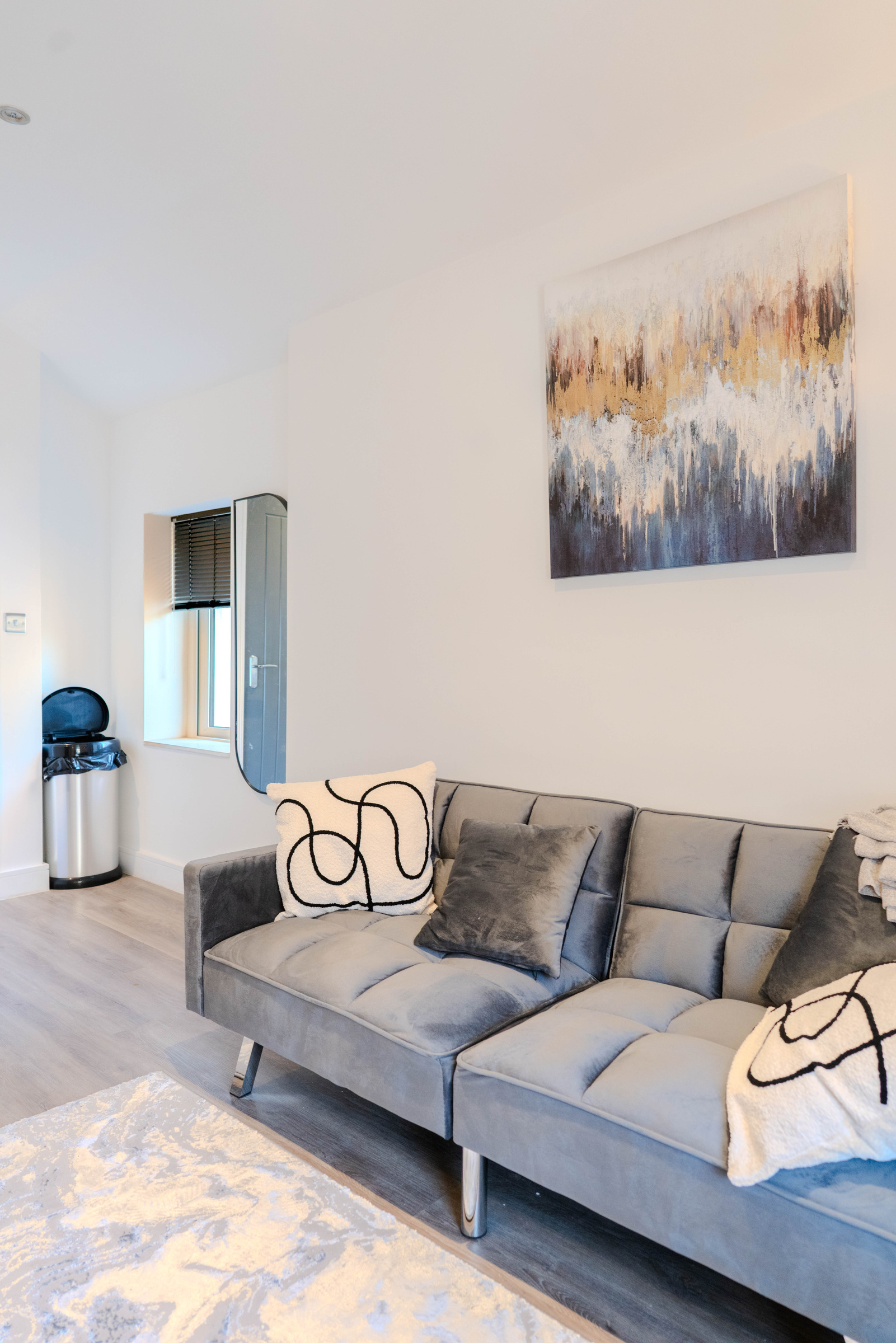 Grey sofa and patterned cushions beneath a framed cityscape print in a bright studio.