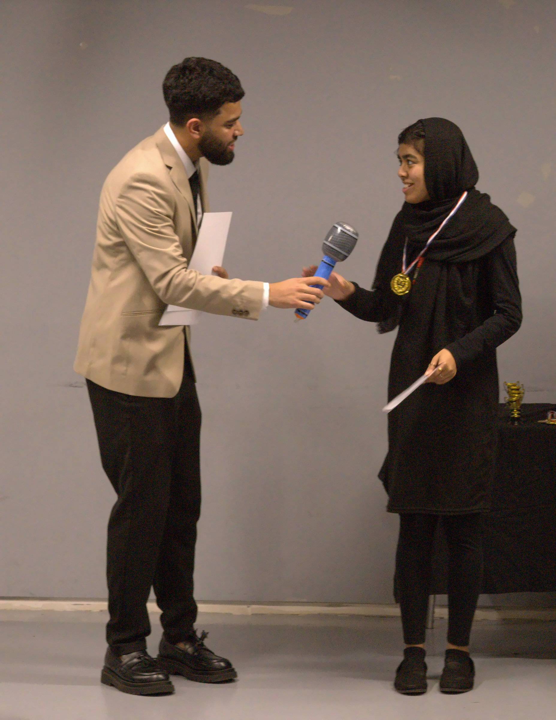 A presenter handing a microphone to an award recipient on stage.