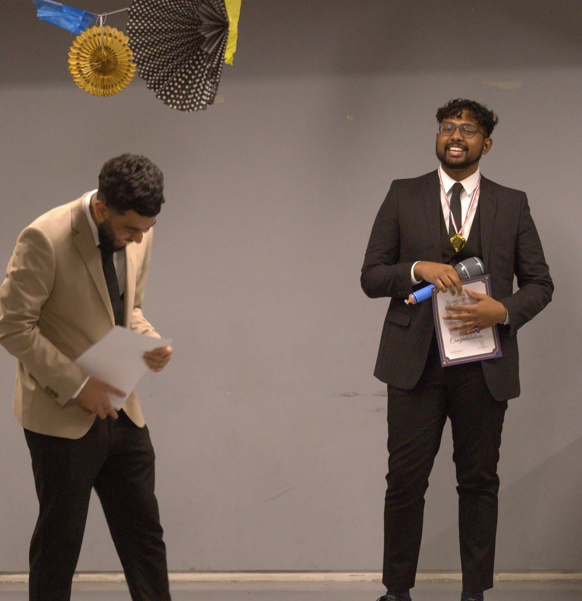 Two presenters sharing a candid laugh during a community awards evening.