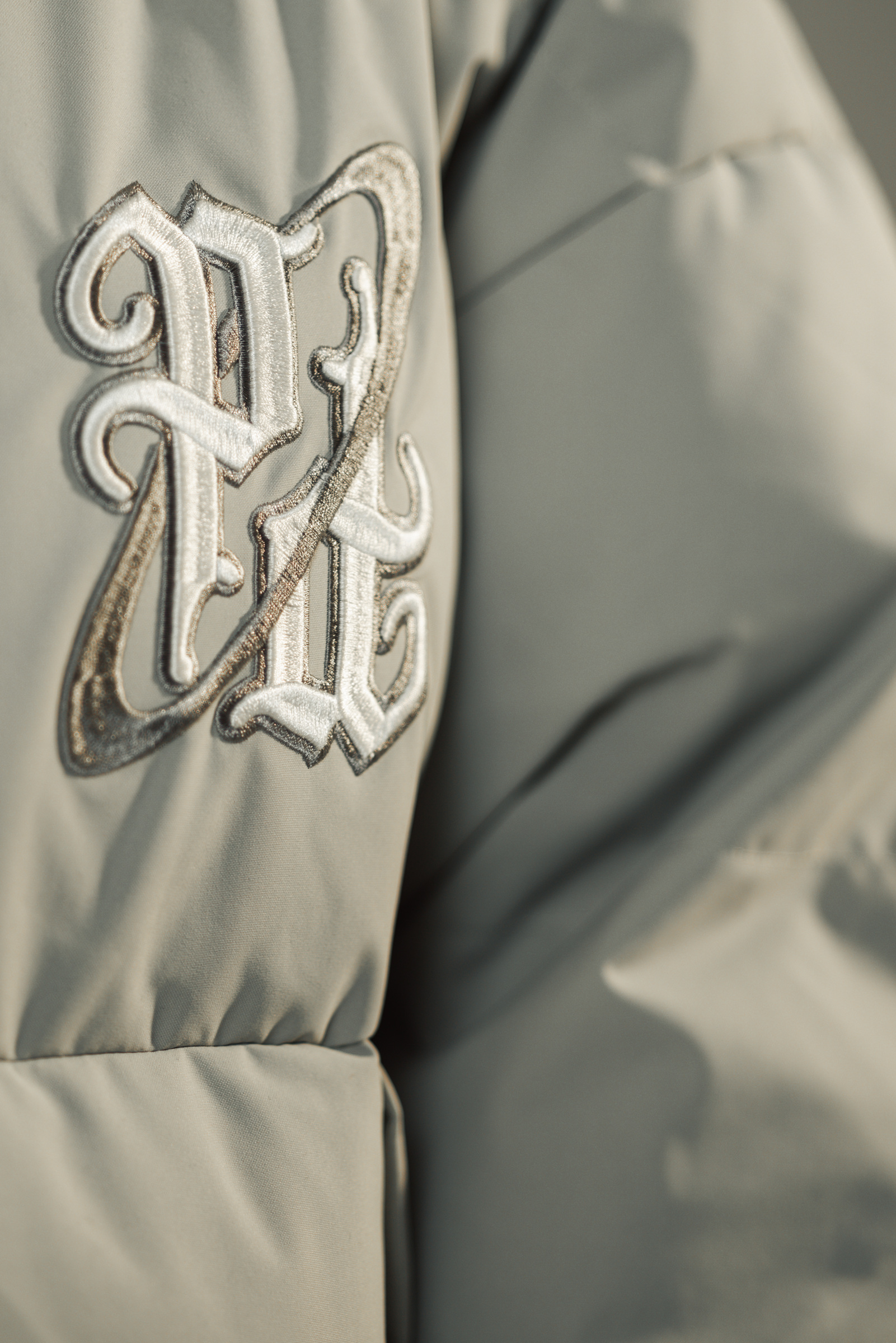 Raised cream and silver embroidery on the pale grey woven fabric of a puffer jacket.