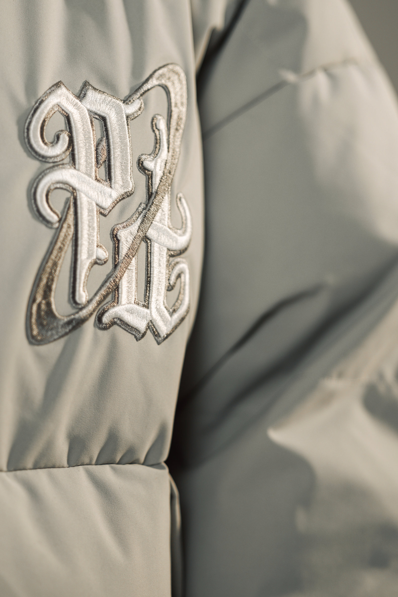 A close photograph of raised embroidered lettering and the fabric of a pale puffer jacket.