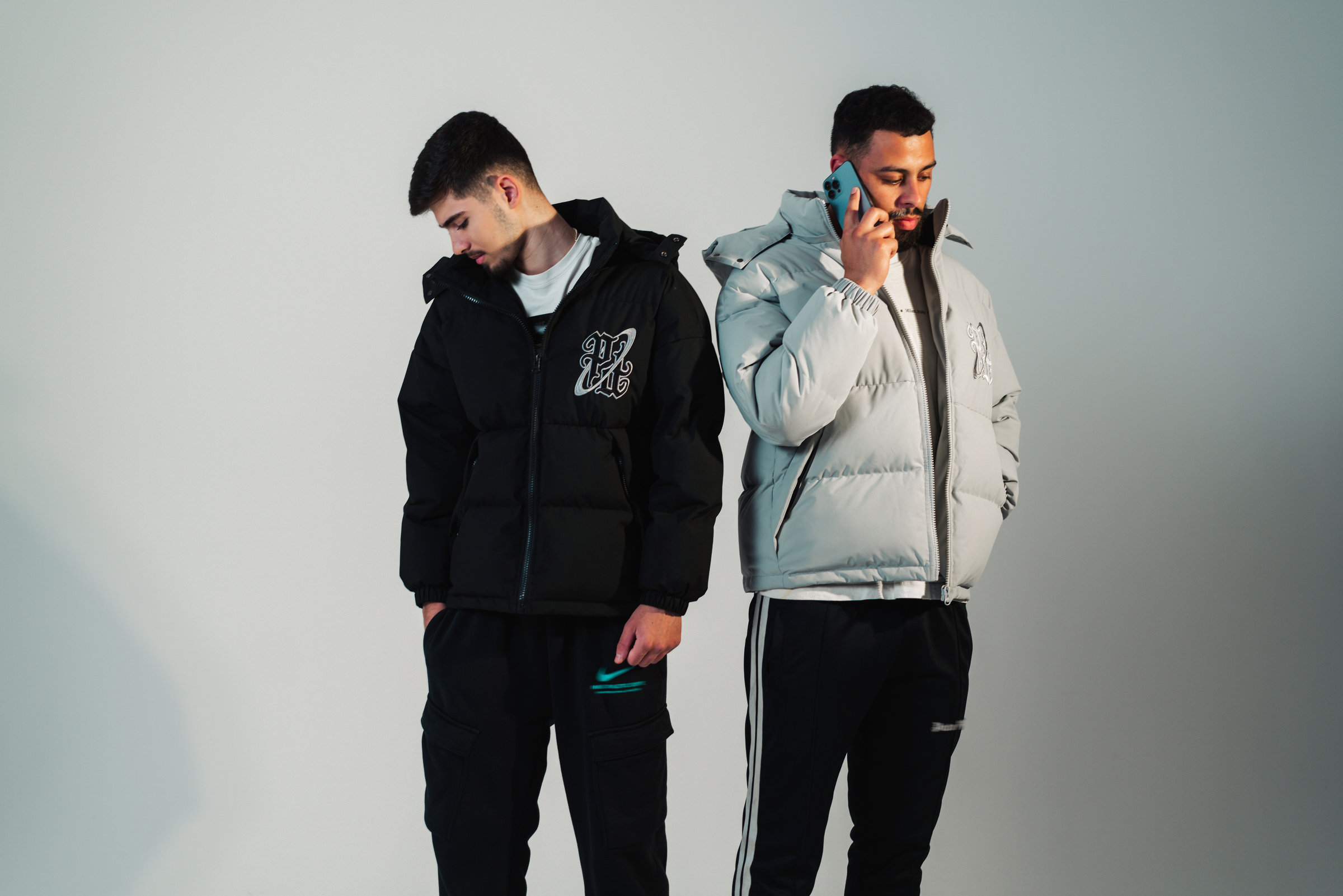 Two models wearing black and pale blue puffer jackets in a studio campaign photograph.