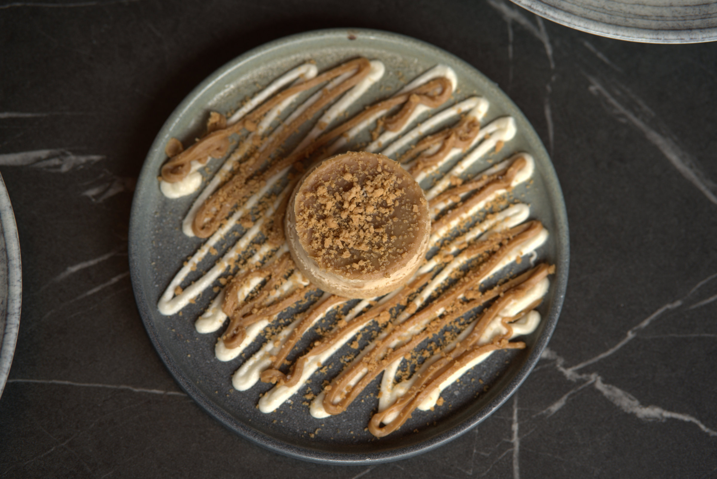 A biscuit-topped dessert with cream and caramel drizzle on a grey plate.