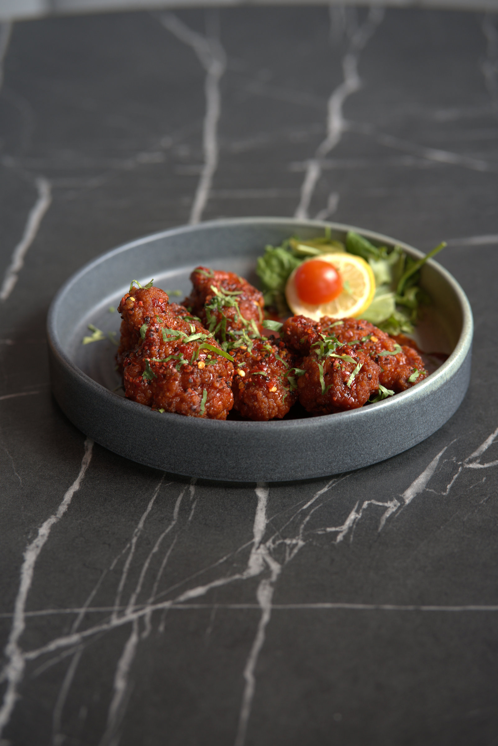 Glazed chicken wings with sesame and spring onion in a grey bowl on a marble table.
