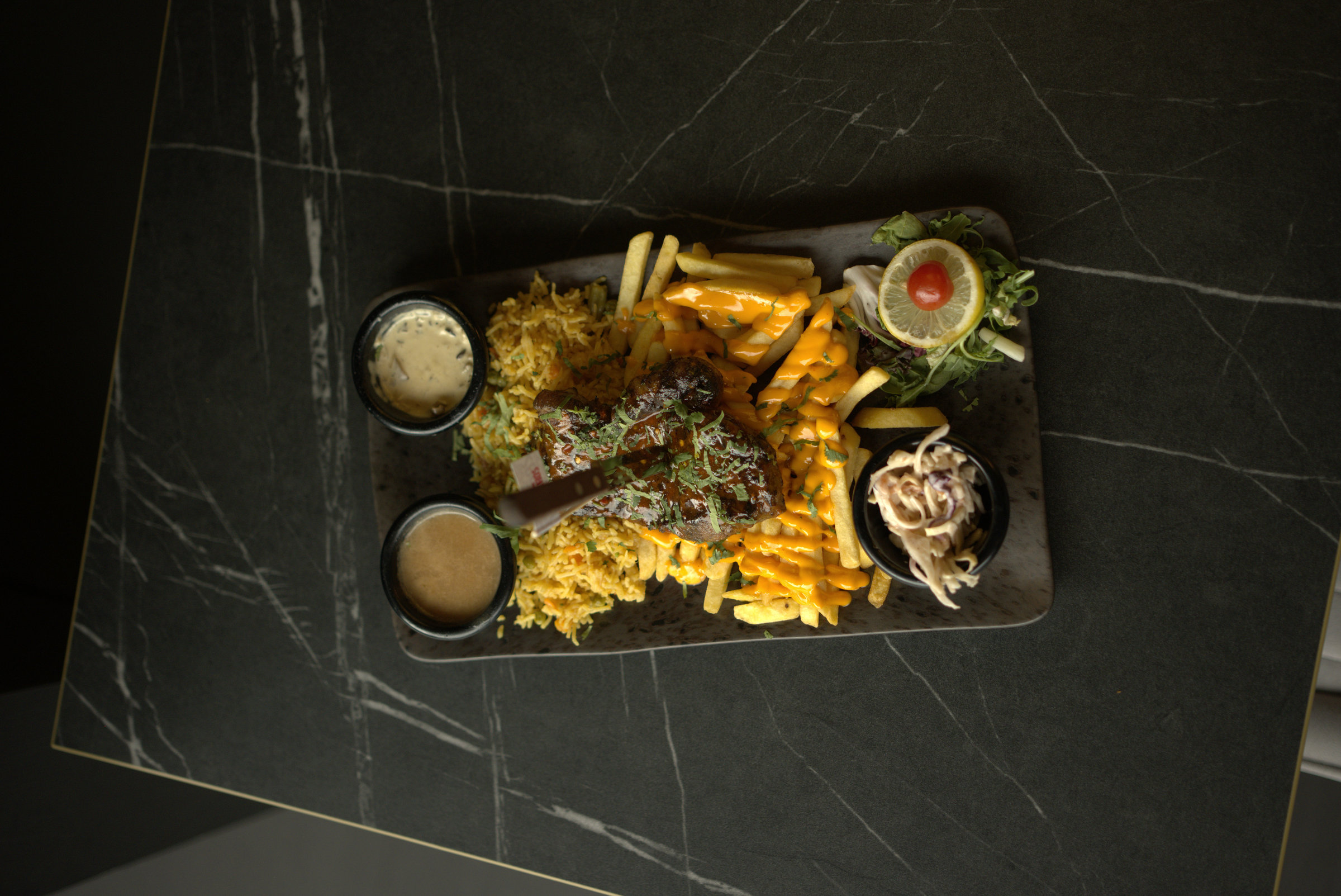 An overhead photograph of a loaded restaurant platter with chicken, rice, fries and dips.