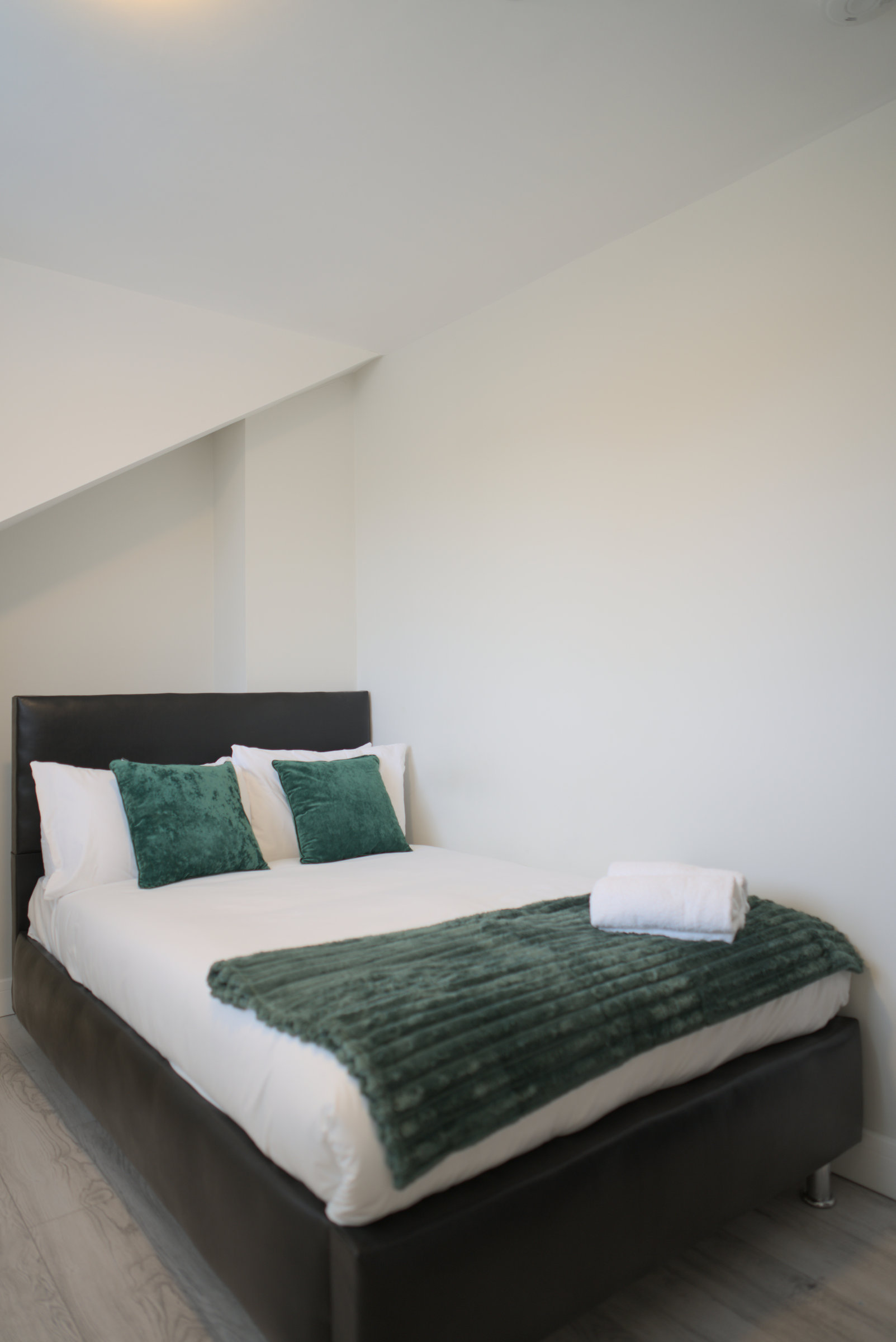 Double bed with green cushions and a folded green throw beneath a sloping loft ceiling.
