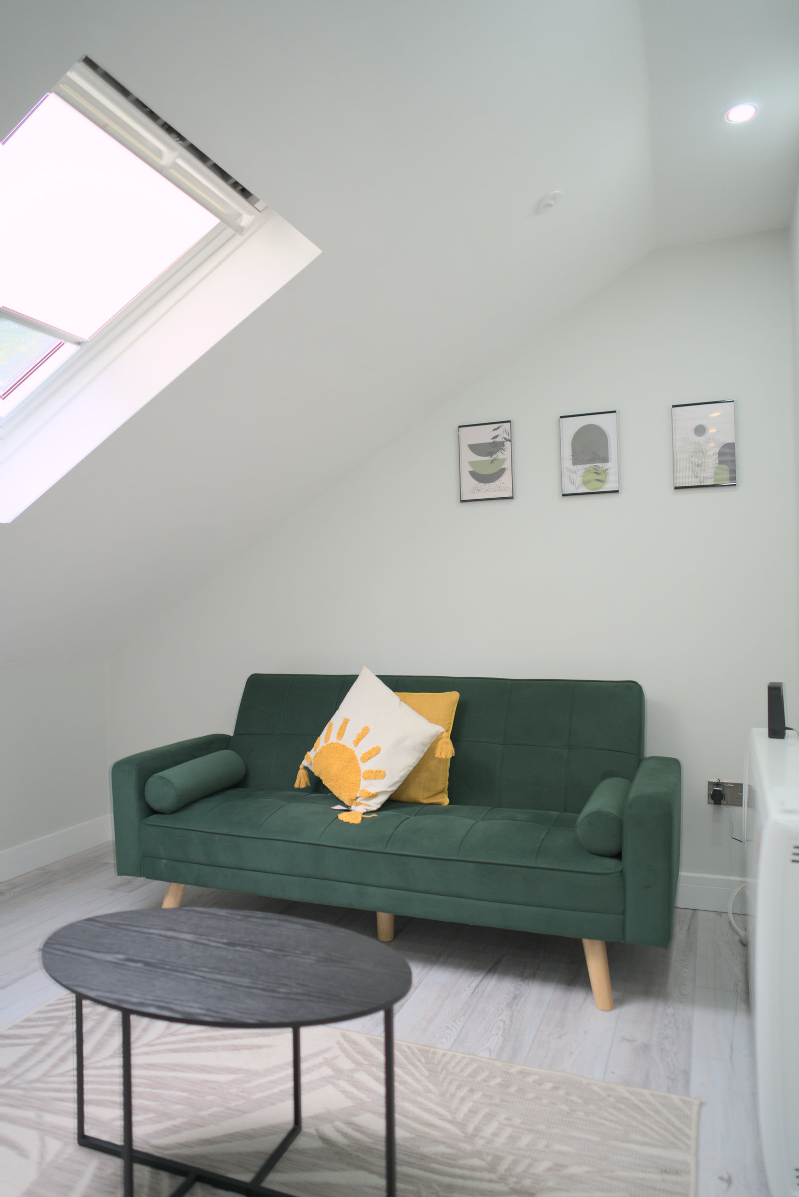 Green velvet sofa, coffee table and framed prints in a daylight-filled loft studio.