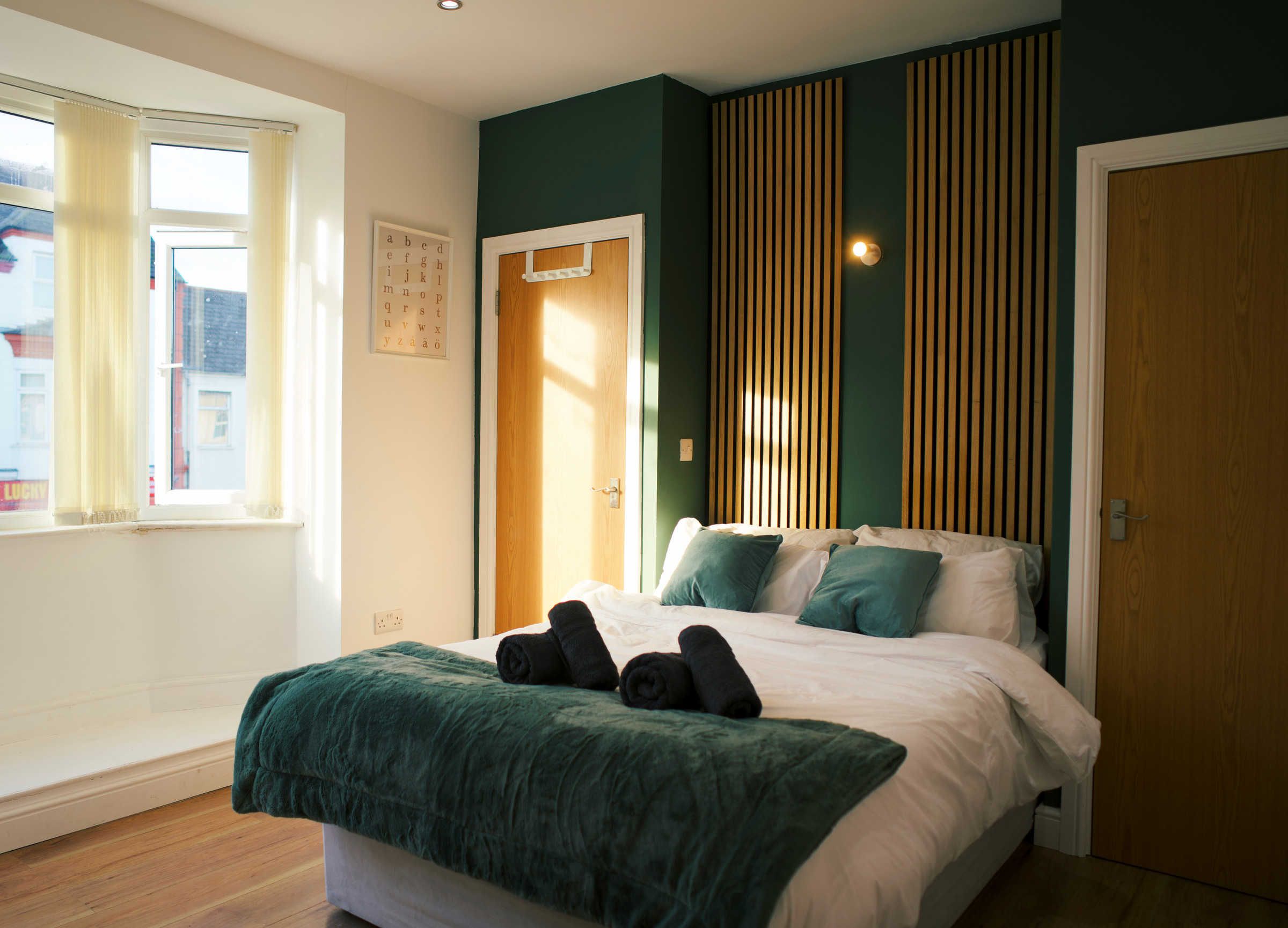 Green bedding and rolled dark towels beside a timber-slat feature wall and sunlit window.