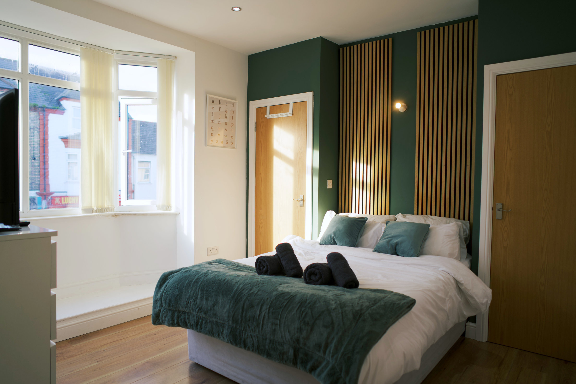 Sunlight across green velvet bed linen, timber wall slats and the actual street-facing window.