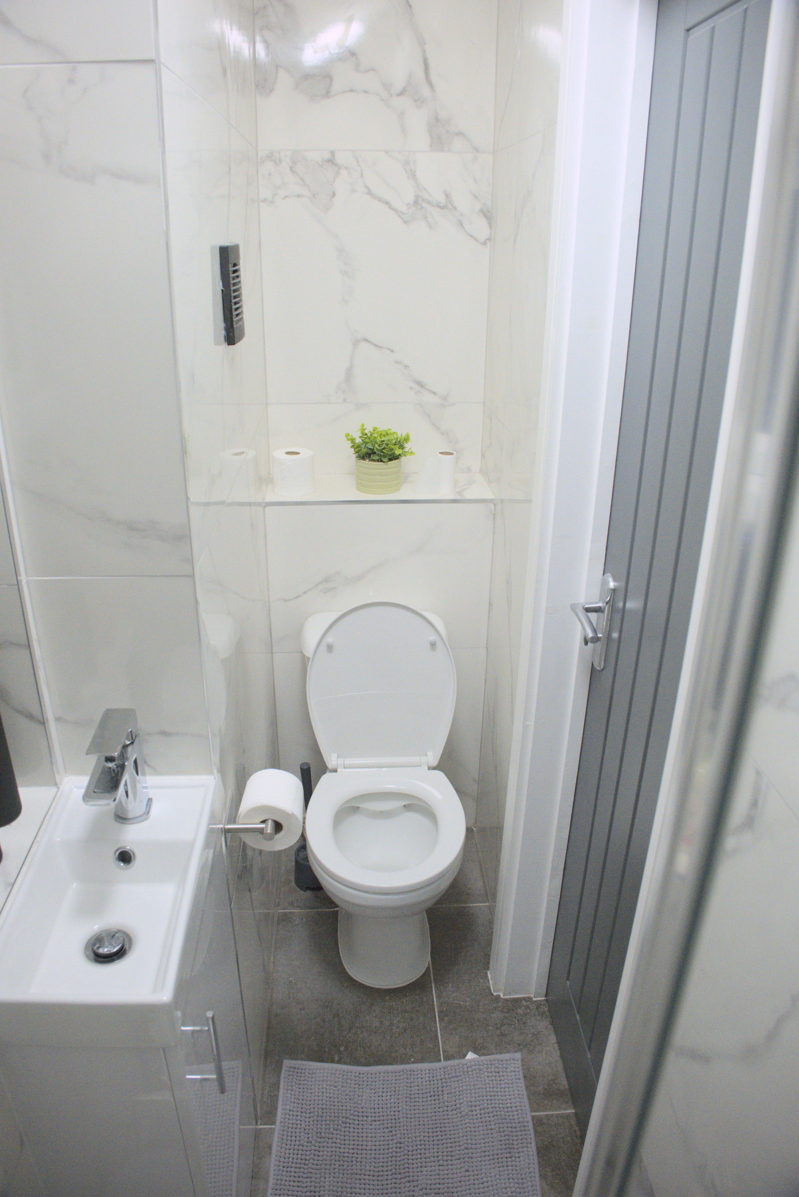 A compact marble-pattern bathroom with white fittings and its original shower.