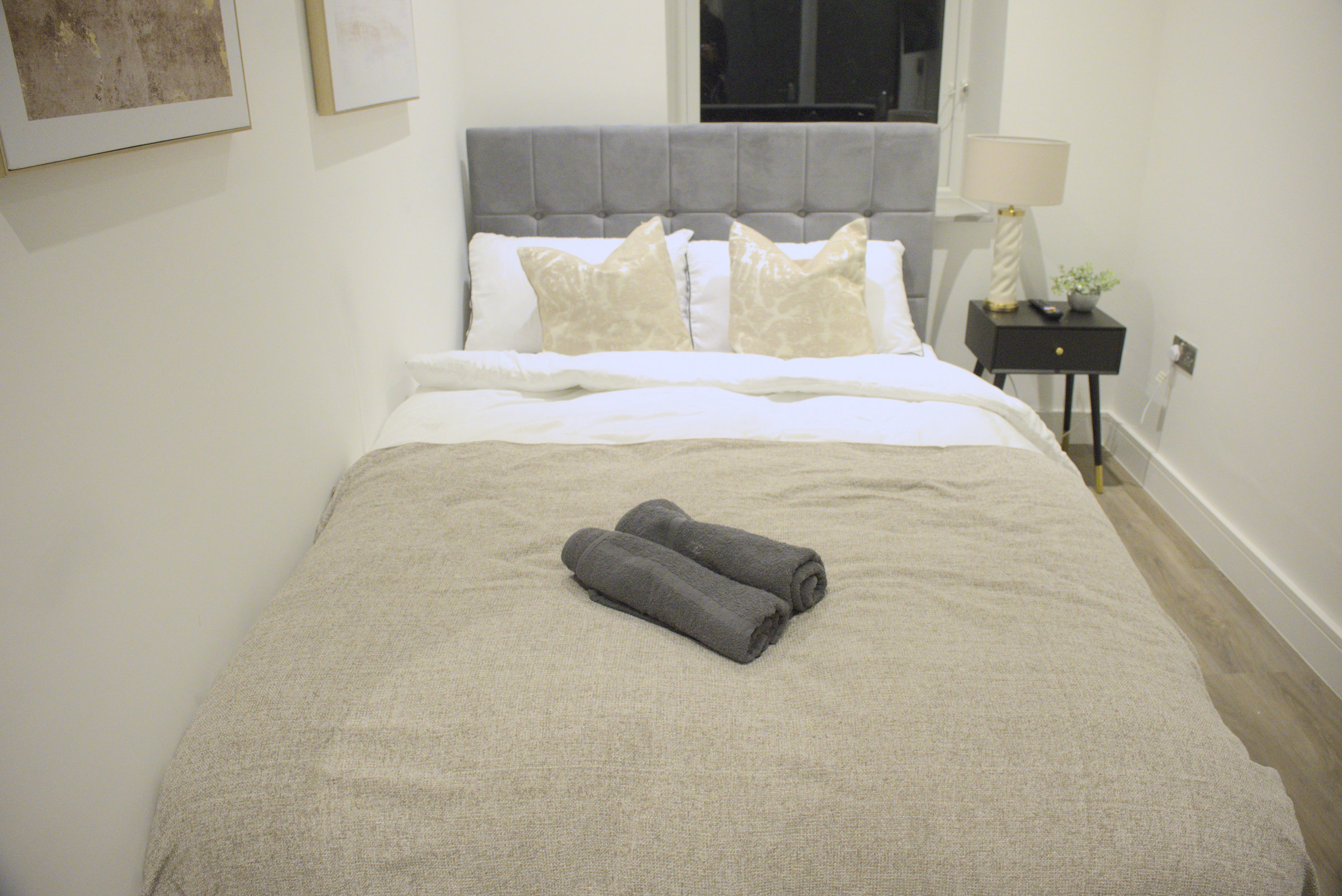 A guest bedroom with an upholstered headboard, white linen and dark folded towels.