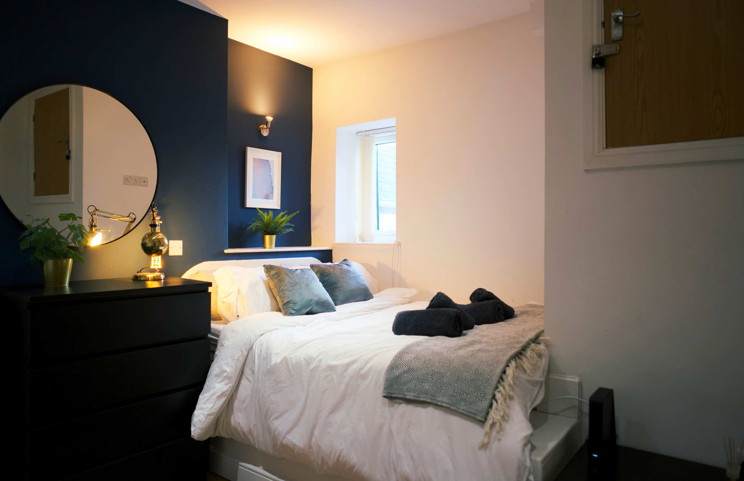 White double bed, navy feature wall and warm brass bedside lights in a compact guest bedroom.