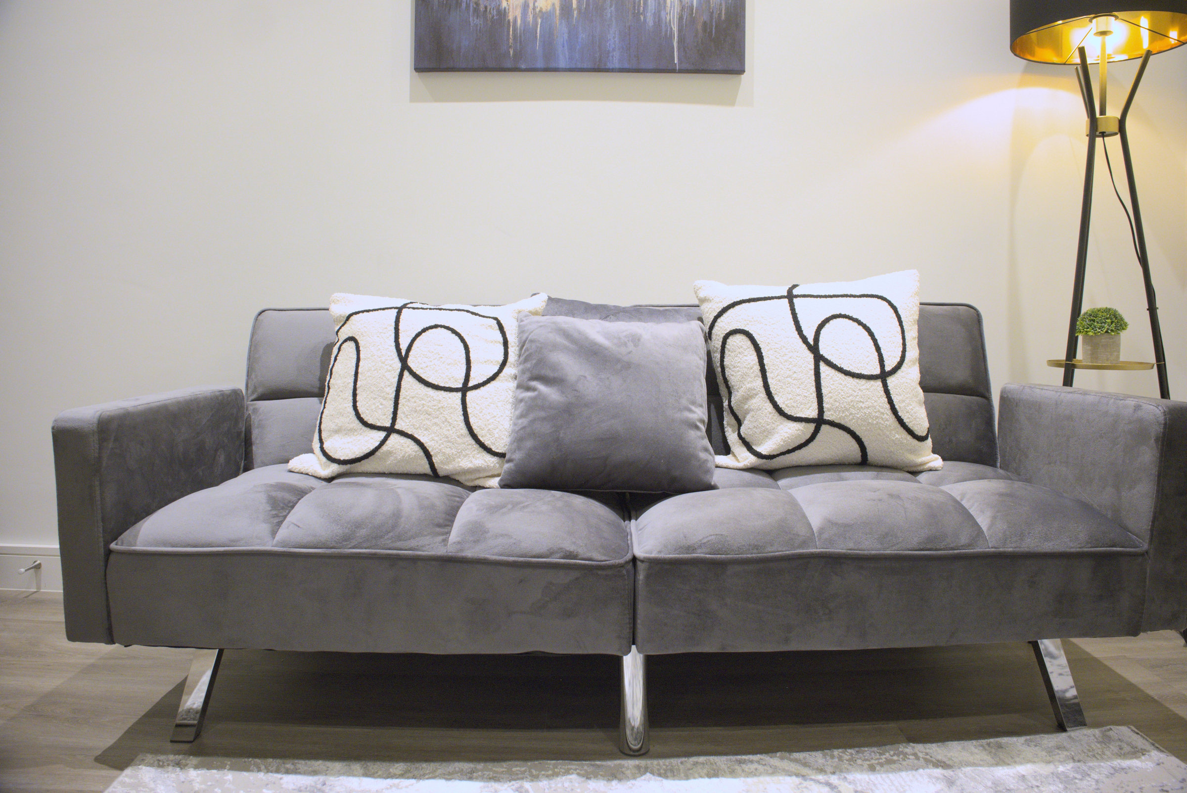 A velvet sofa with patterned cushions, framed art and a brass floor lamp.