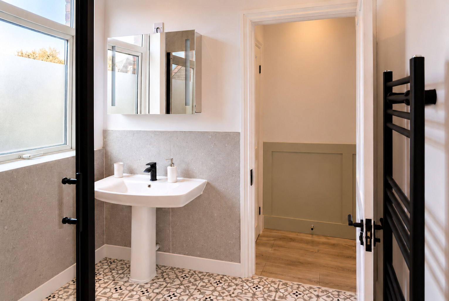 White basin, mirror and black heated towel rail viewed from the shower.