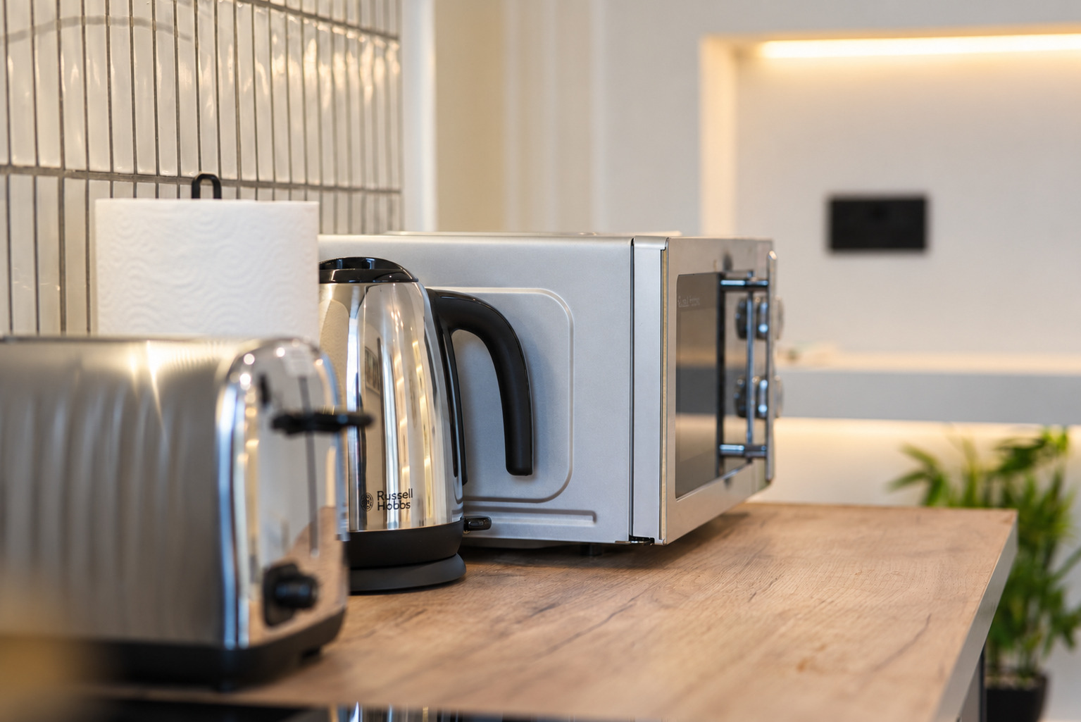 Kettle, toaster and microwave on a wood kitchen counter with soft focus beyond.