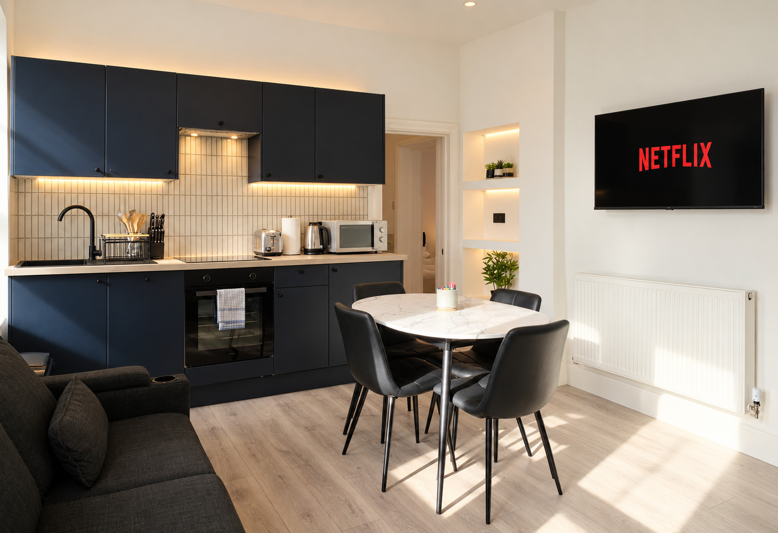 Dark fitted kitchen and round dining table with sunlight crossing the floor.