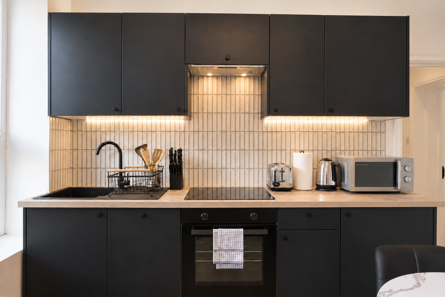 Straight view of dark kitchen cabinets, wood worktop, sink, hob and oven.
