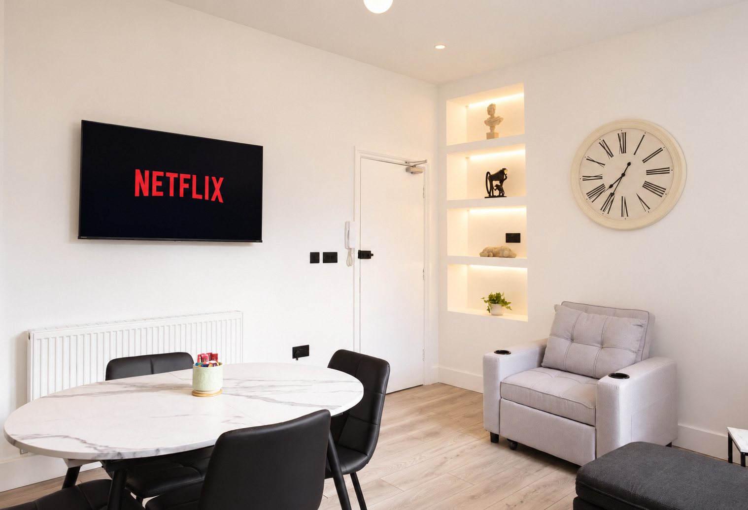 Round dining table, grey chair and illuminated display niches on the reverse lounge wall.