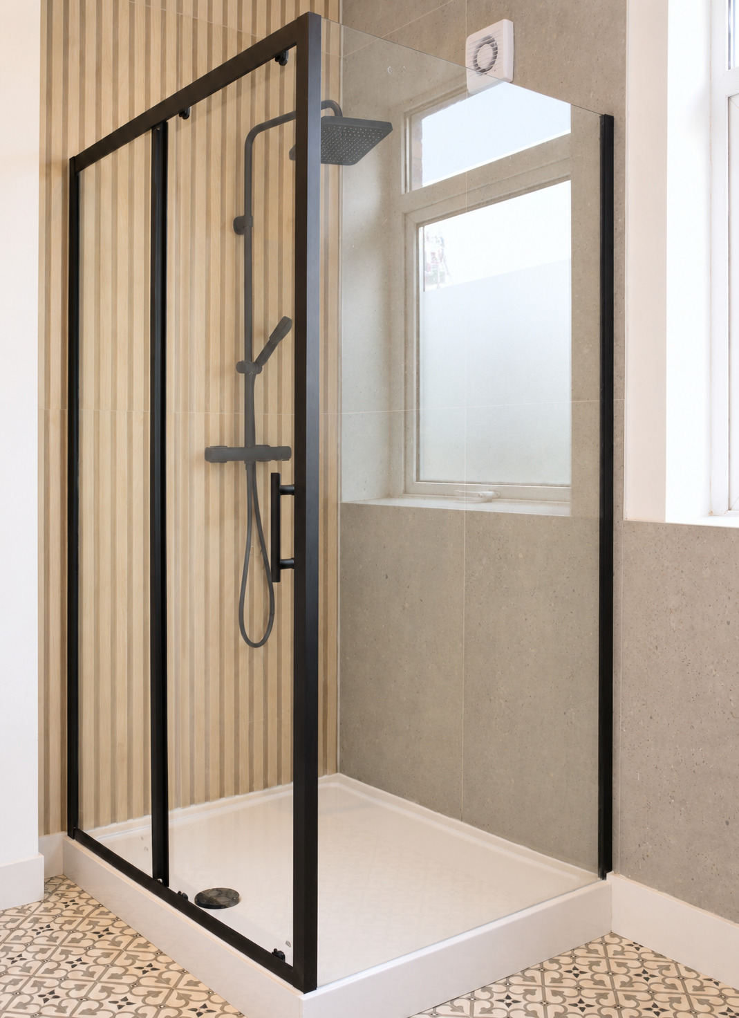Portrait view of a black-framed shower enclosure beside a bright bathroom window.