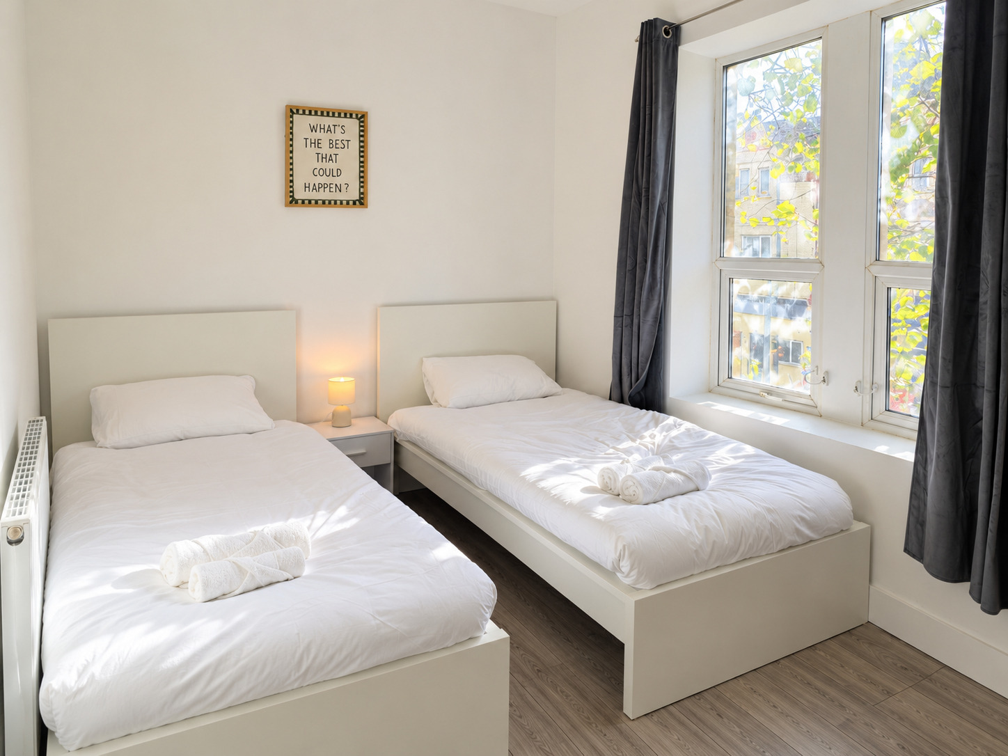 Two white single beds, rolled towels and daylight through the adjoining window.
