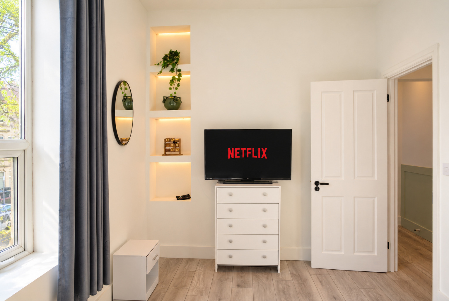 Bedroom drawers and television beside illuminated niches and the doorway.