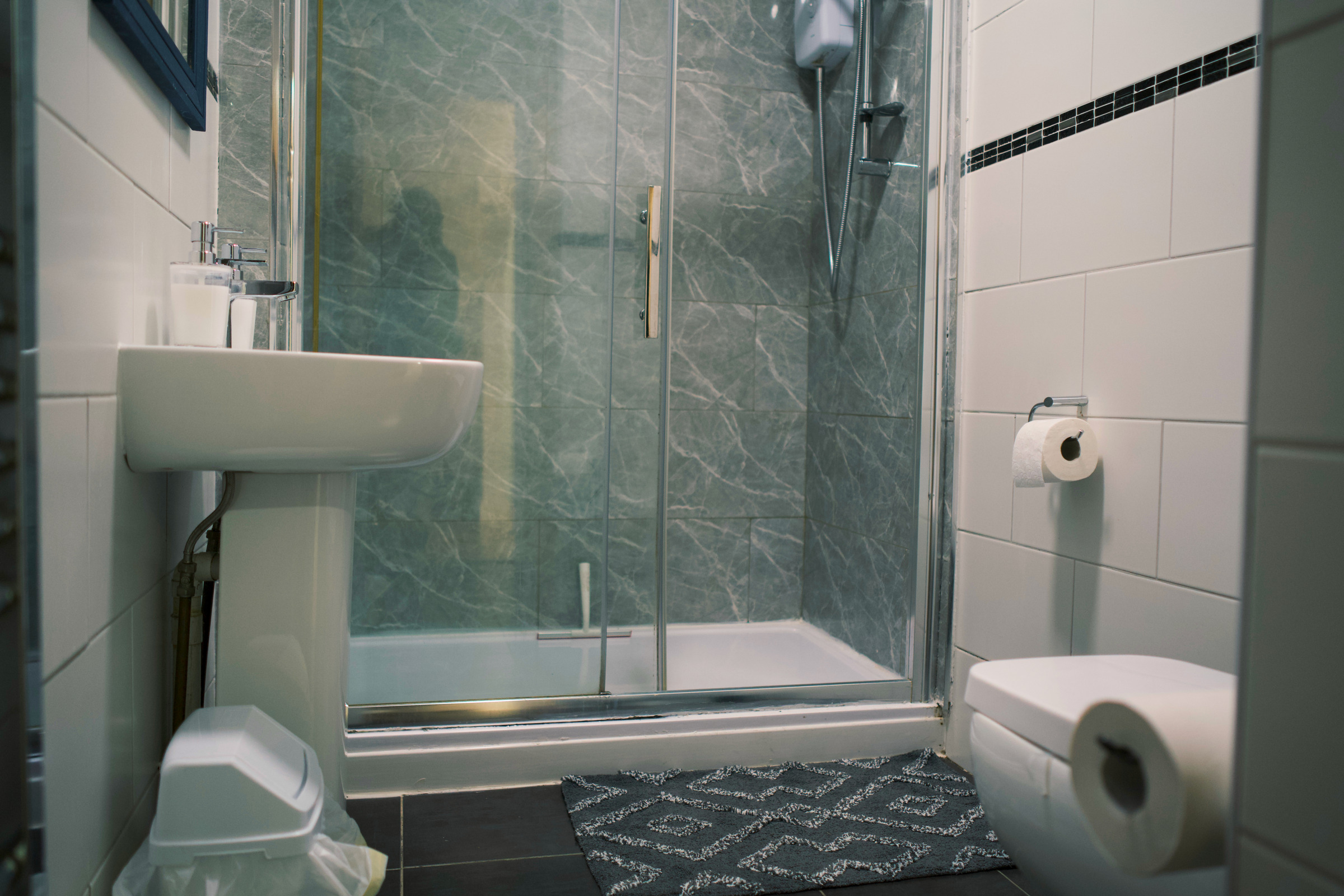 Glass shower enclosure, white basin and toilet in a compact grey stone-tiled bathroom.
