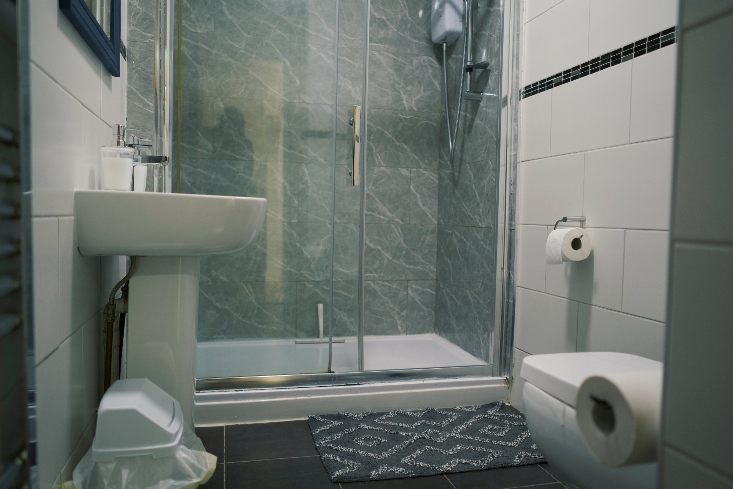 The original stone-tiled shower, white basin and toilet in an apartment bathroom.