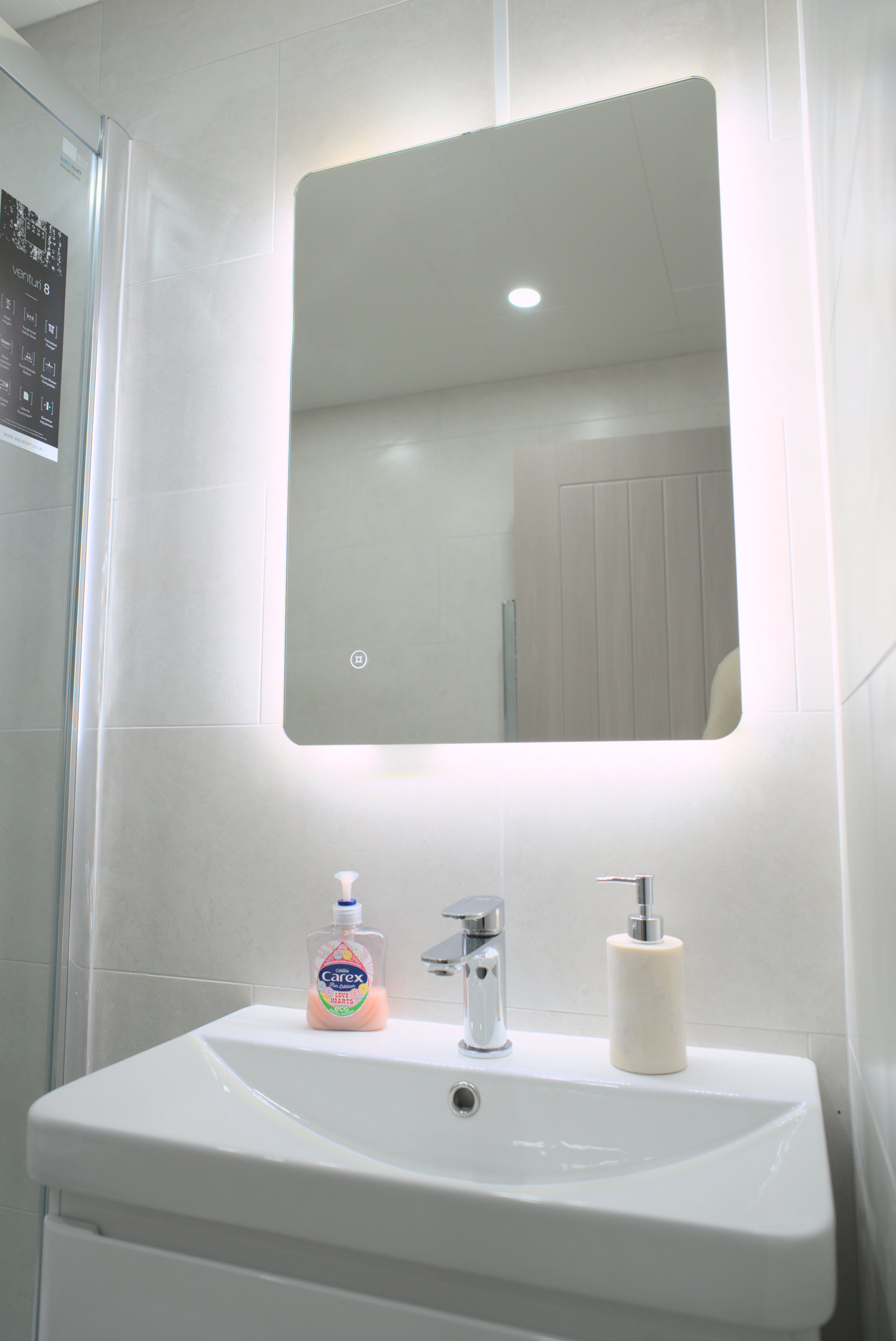 A white basin and illuminated bathroom mirror, with the real tiled finish.