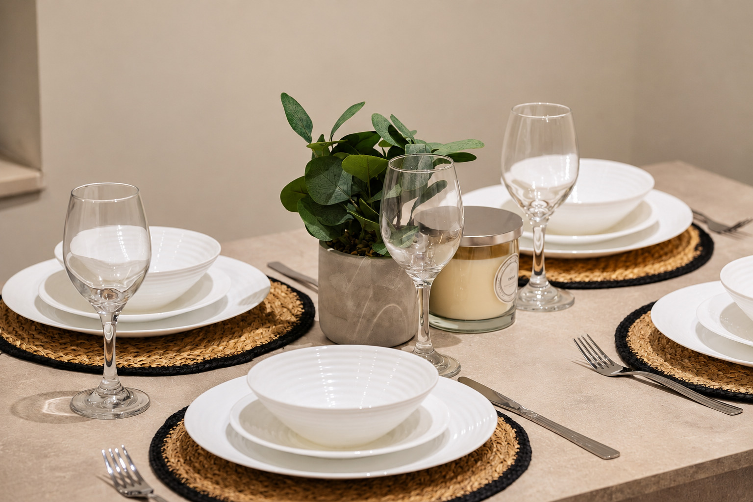 White tableware, clear glasses and woven placemats around a green plant on a dining table.