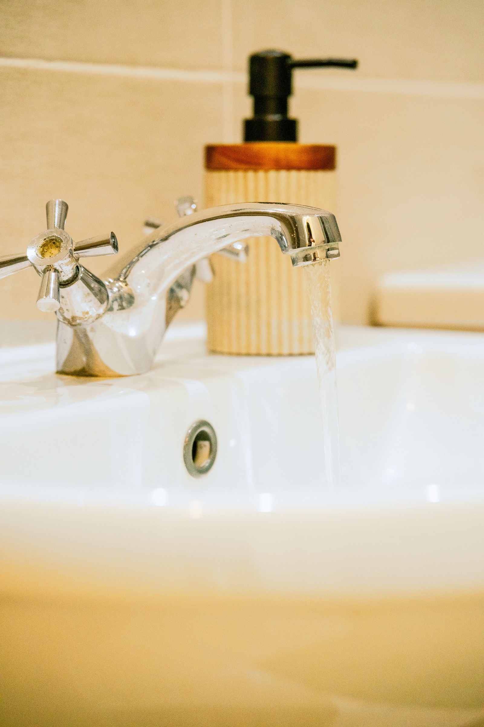 Chrome bathroom tap, white basin and soap dispenser in a close detail.