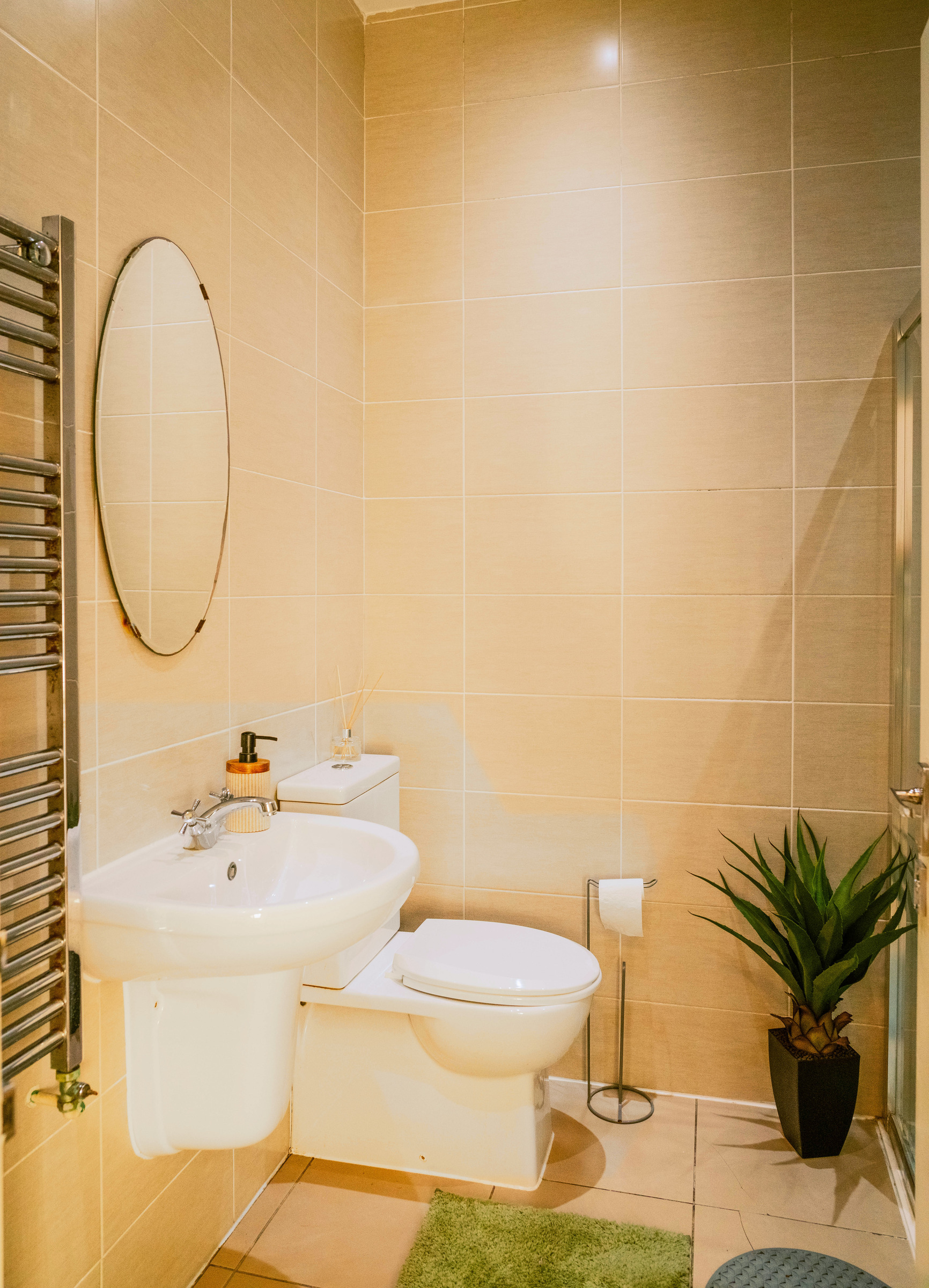 Compact tiled bathroom with basin, toilet, round mirror and shower enclosure.