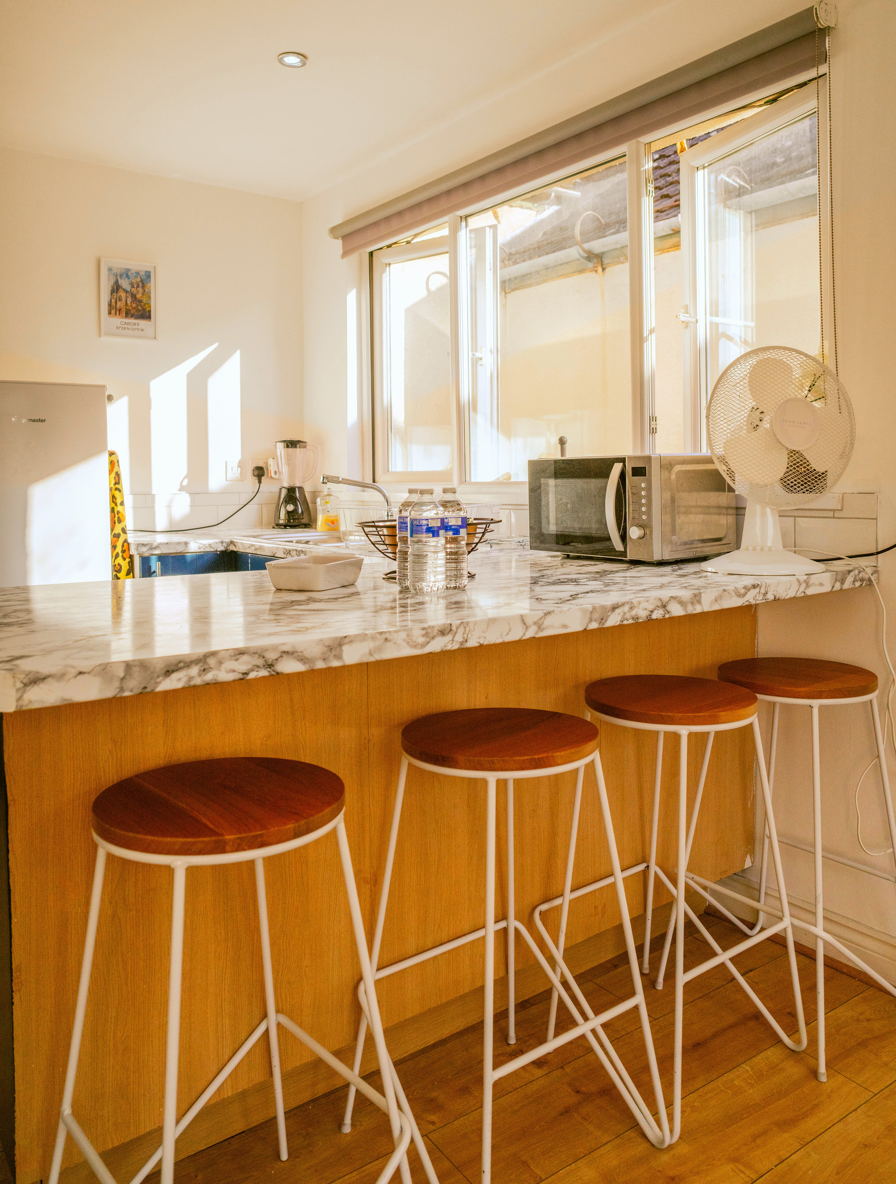 Two stools at a marble-pattern breakfast counter beside a sunlit kitchen window.